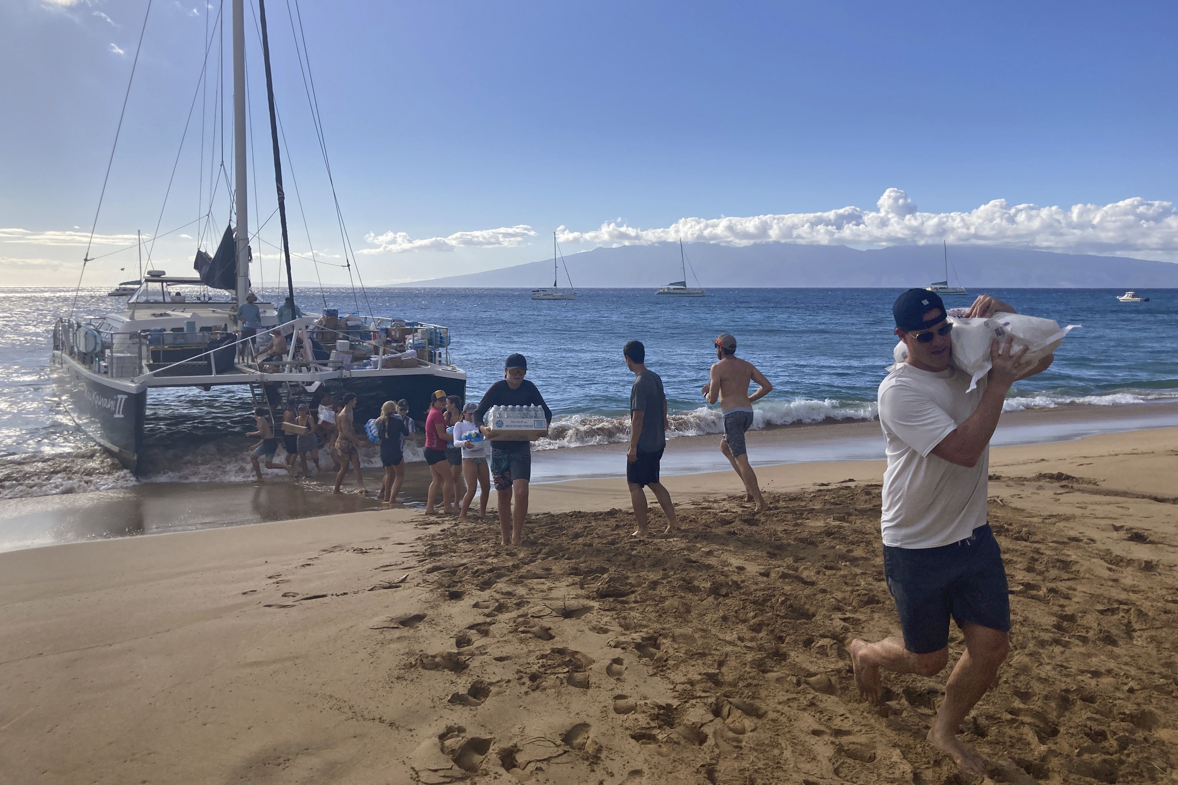 Un grupo de voluntarios que navegó desde la bahía de Maalaea, Maui, forma una línea de montaje en la playa de Kaanapali para descargar las donaciones de un barco. (AP Foto/Rick Bowmer)