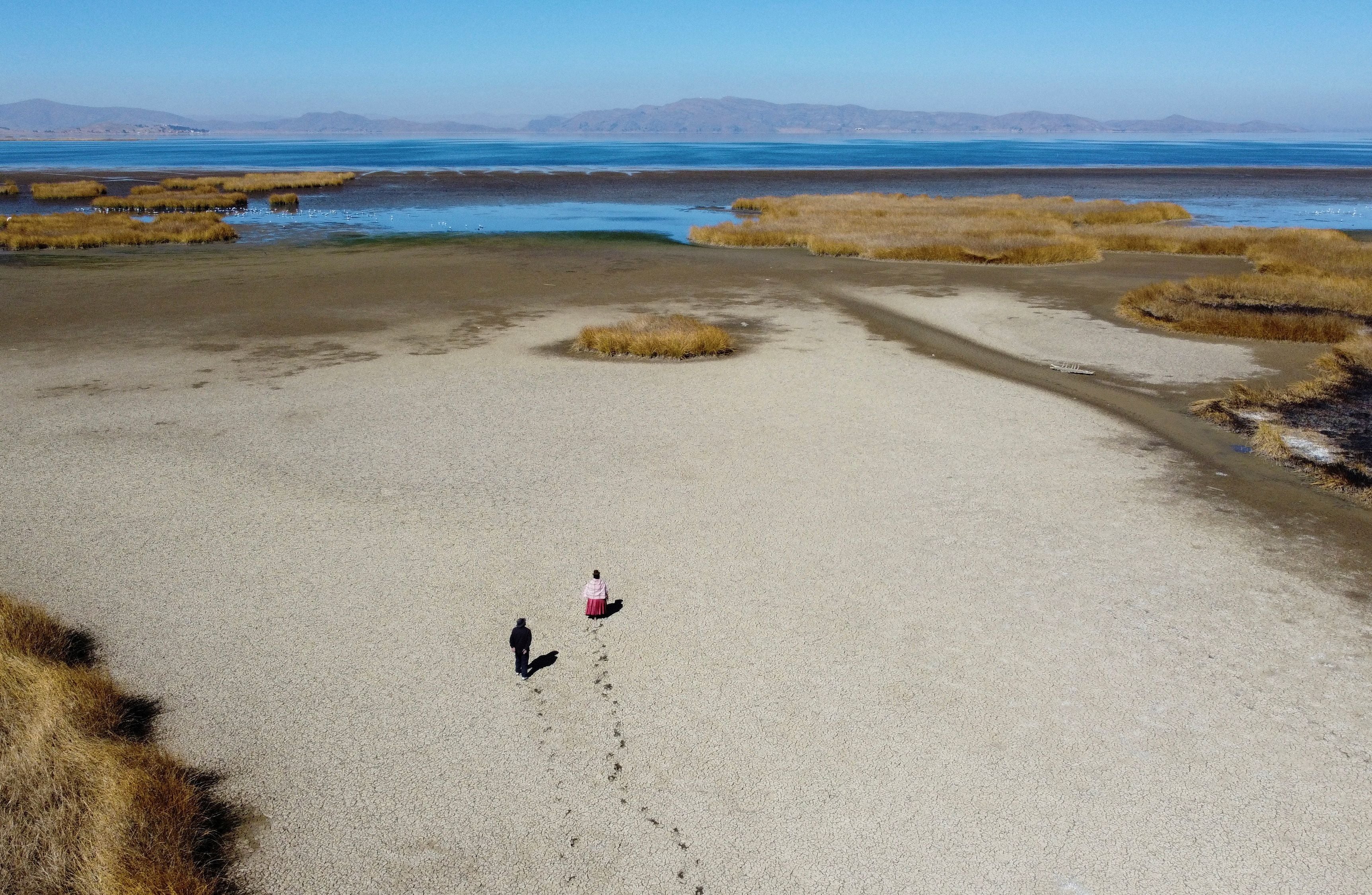 Dos pobladores caminan sobre el lecho seco y agrietado cerca de la orilla del lago Titicaca en la temporada de sequía en Huarina, Bolivia. REUTERS/Claudia Morales