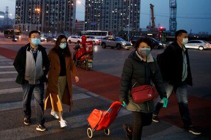 Grupo de personas con máscaras faciales frente a un centro comercial en Pekín mientras el país es golpeado por un brote de coronavirus