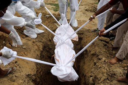 Personas vestidas con trajes protectores bajan el cuerpo de una mujer que murió de COVID-19 en Nueva Delhi, India, el 7 de agosto de 2020 (REUTERS/Adnan Abidi)