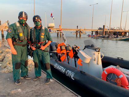 Los guardias civiles Juan Salinero y José Madrid, junto a la lancha neumática que la Guardia Civil tiene desde hace 15 días en Gambia,  que contrastan con los pequeños fuera borda de las barcazas de madera en el muelle de la Armada gambiana, donde conviven pescadores locales, buques de guerra y pesqueros chinos. EFE/María Traspaderne
