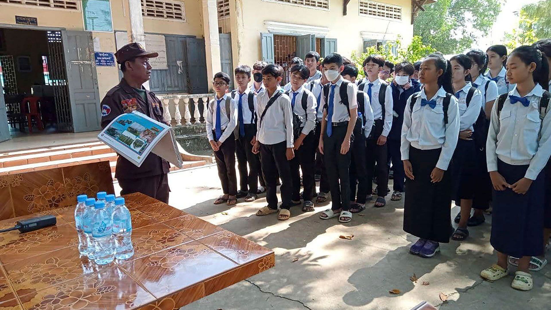 En esta foto publicada por el Centro de Acción contra las Minas de Camboya, CMAC, un experto en remoción de minas, a la izquierda, explica a los estudiantes de la escuela secundaria Queen Kosamak en la provincia de Kratie, al noreste de Phnom Penh, Camboya, el domingo 13 de agosto de 2023.  (Centro de Acción contra las Minas de Camboya vía AP)

