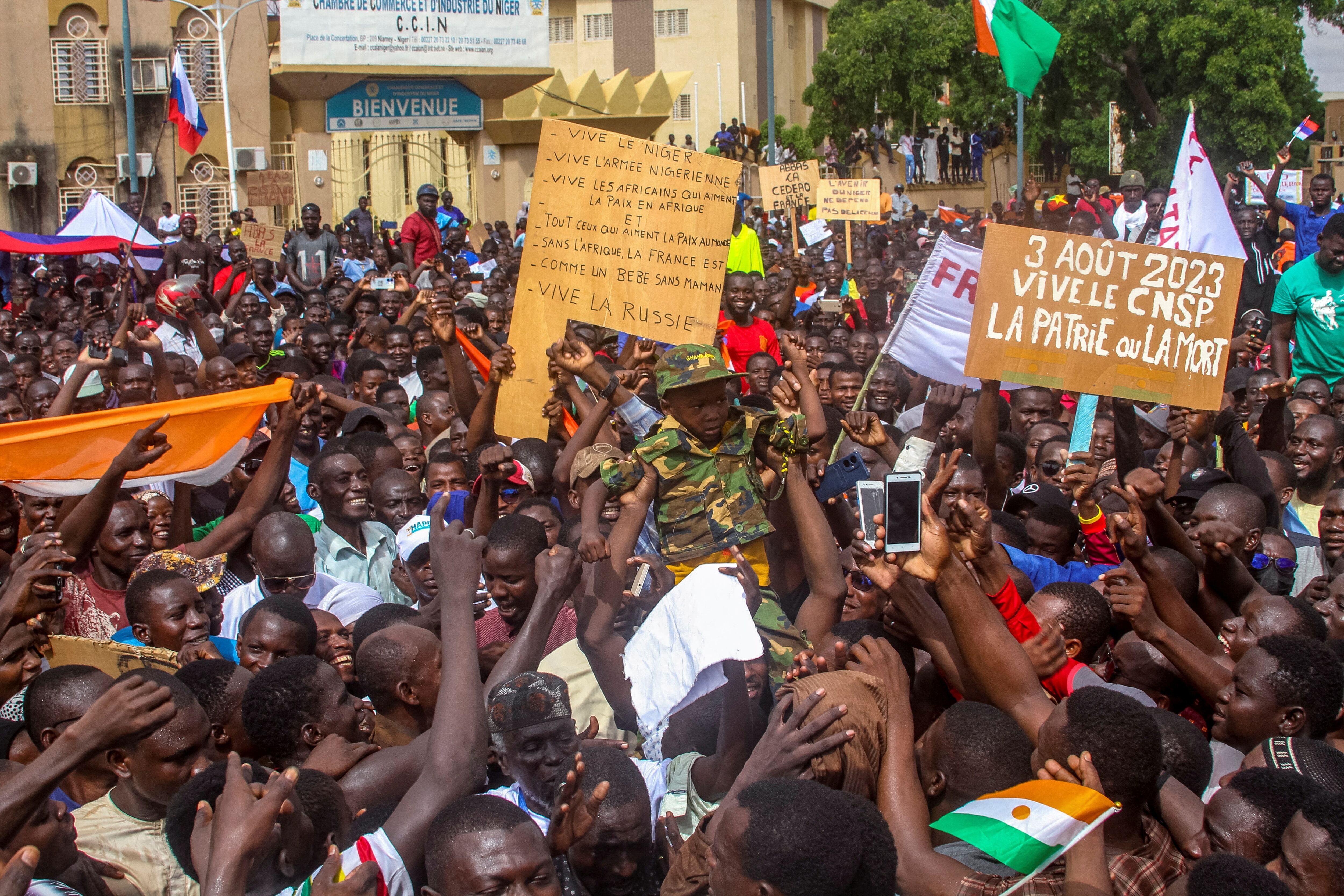 Personas sostienen a un niño vestido con uniforme militar mientras se reúnen con miles de manifestantes contra las sanciones en apoyo a los soldados golpistas en la capital Niamey, Níger 3 de agosto 2023. REUTERS/Mahamadou Hamidou 