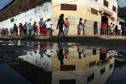 Vecinos en fila para recibir alimentos básicos gratuitos ante la escuela primaria de Santa Ana, en Asunción, Paraguay, proporcionados por un programa del Ministerio de Educación, durante las cuarentenas contra el COVID-19, el martes 31 de marzo de 2020.  (AP Foto/Jorge Sáenz)
