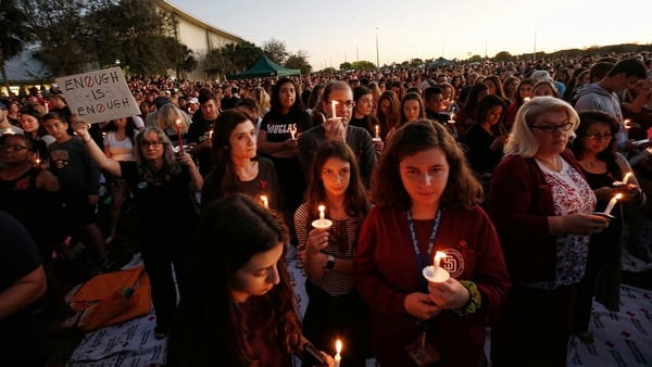 Miles de personas sostienen velas durante una vigilia con velas para las víctimas de la balacera Marjory Stoneman Douglas High School en Parkland, Florida. “Suficiente es suficiente”, afirma la pancarta (AFP)