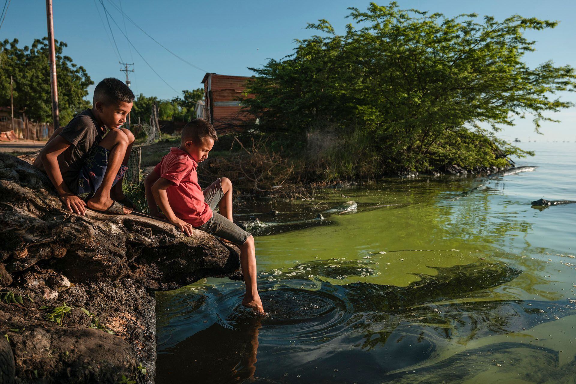 Luis Javier, de 9 años, y Luis David, de 8, juegan a orillas del lago de Maracaibo, el cual además de estar cubierto de petróleo también se ha llenado de algas (NYT)