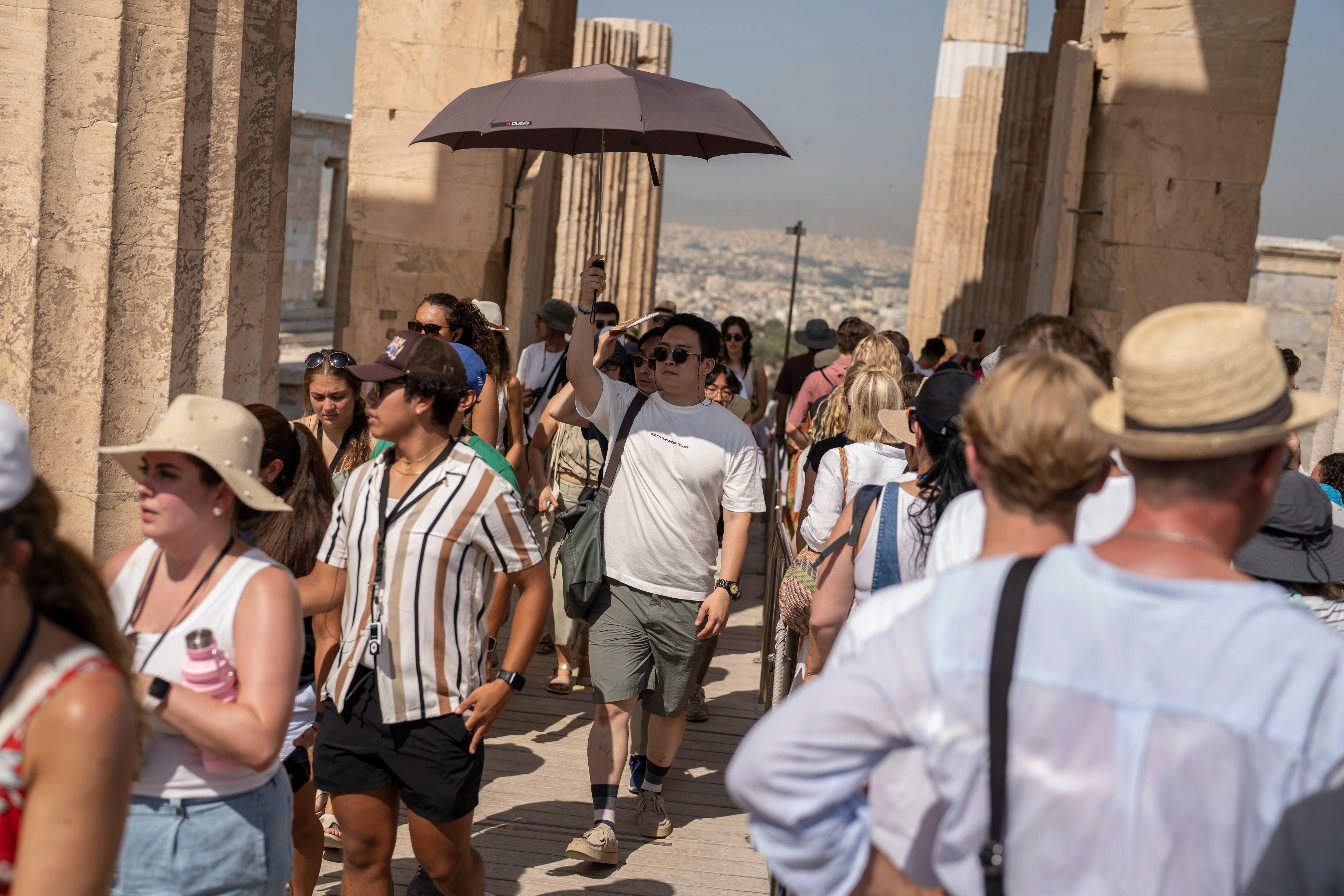 Un hombre sostiene una sombrilla mientras él y otros turistas ingresan a la antigua Acrópolis durante una ola de calor, en Atenas, Grecia, el jueves 13 de julio de 2023. (AP Foto/Petros Giannakouris)