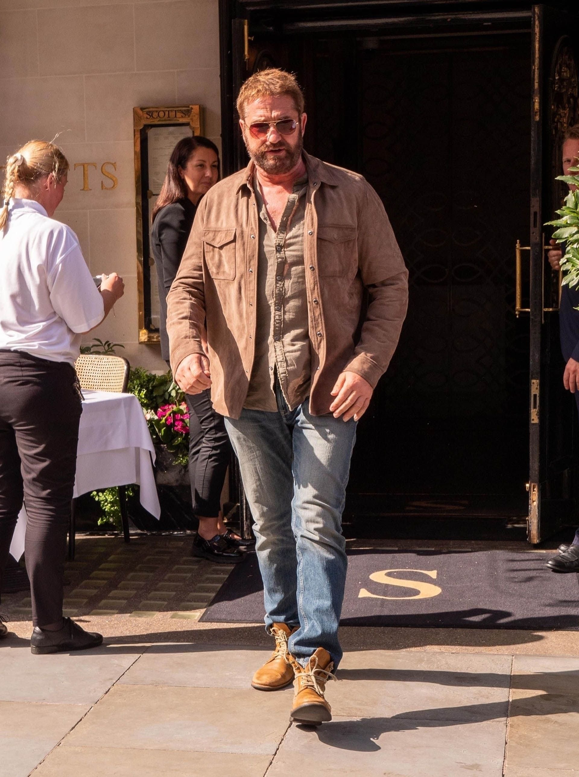 Gerard Butler fue fotografiado cuando salía de un restaurante en Londres (Inglaterra) en el que compartió un almuerzo al aire libre aprovechando el buen clima y que la temperatura lo acompañó. El actor vistió una camisa marrón que combinó con su campera y borcegos y un jean. Además, llevó lentes de sol espejados (The Grosby Group)