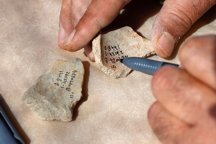 Un trabajador marca números de referencia en fragmentos de cerámica desenterrados en el sitio arqueológico (JACK GUEZ / AFP)