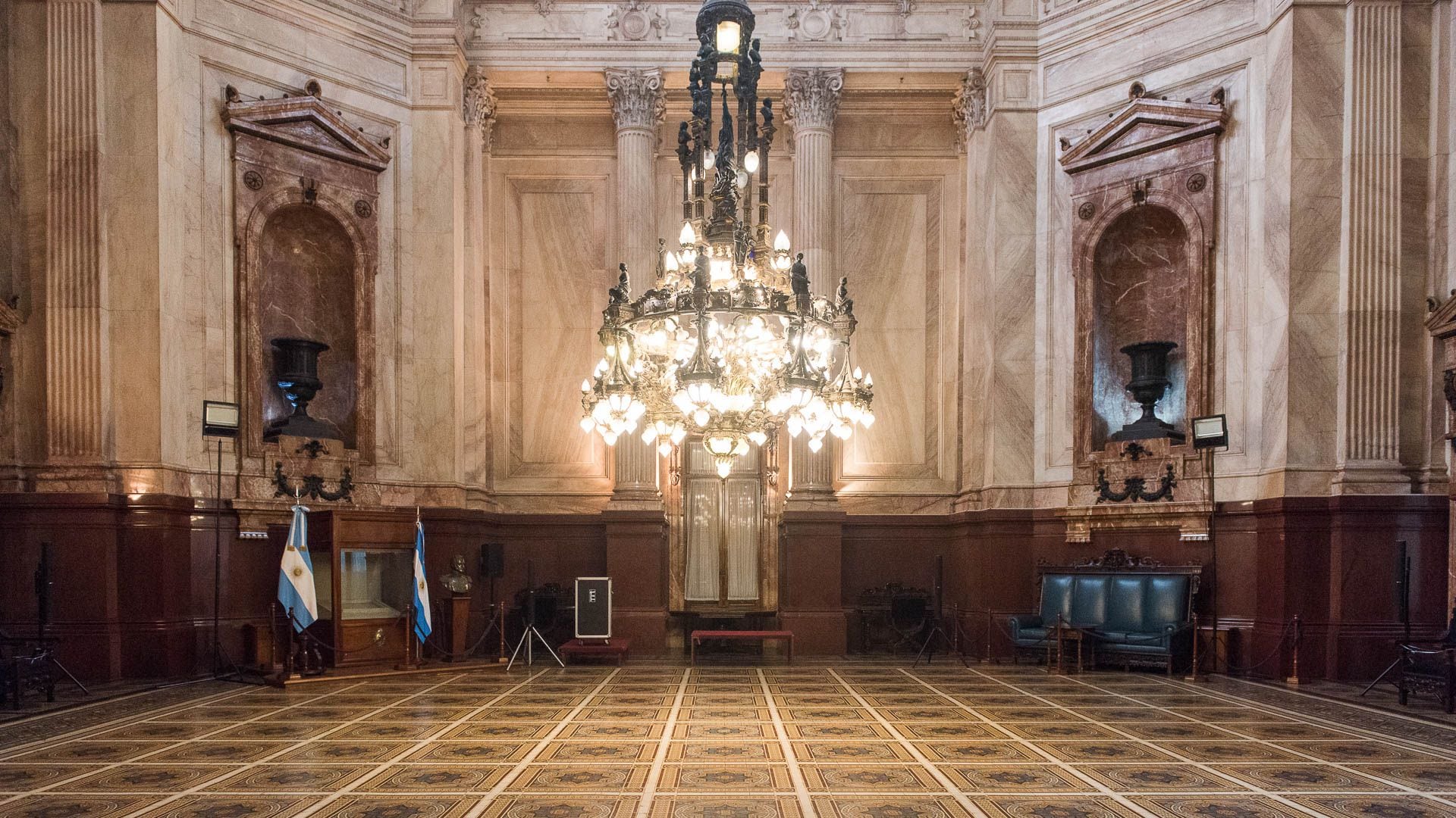 El salón tiene una planta de ocho lados que sostiene la cúpula del Palacio, cuatro pares de columnas de mármol que jerarquizan los accesos, un piso con mosaicos alemanes artísticamente decorados, finos mármoles aplicados a los muros, un zócalo de granito rojo de Bélgica en su base y cuatro nichos de mármol rosa de Alicante que alojan enormes jarrones de bronce (Gustavo Gavotti)