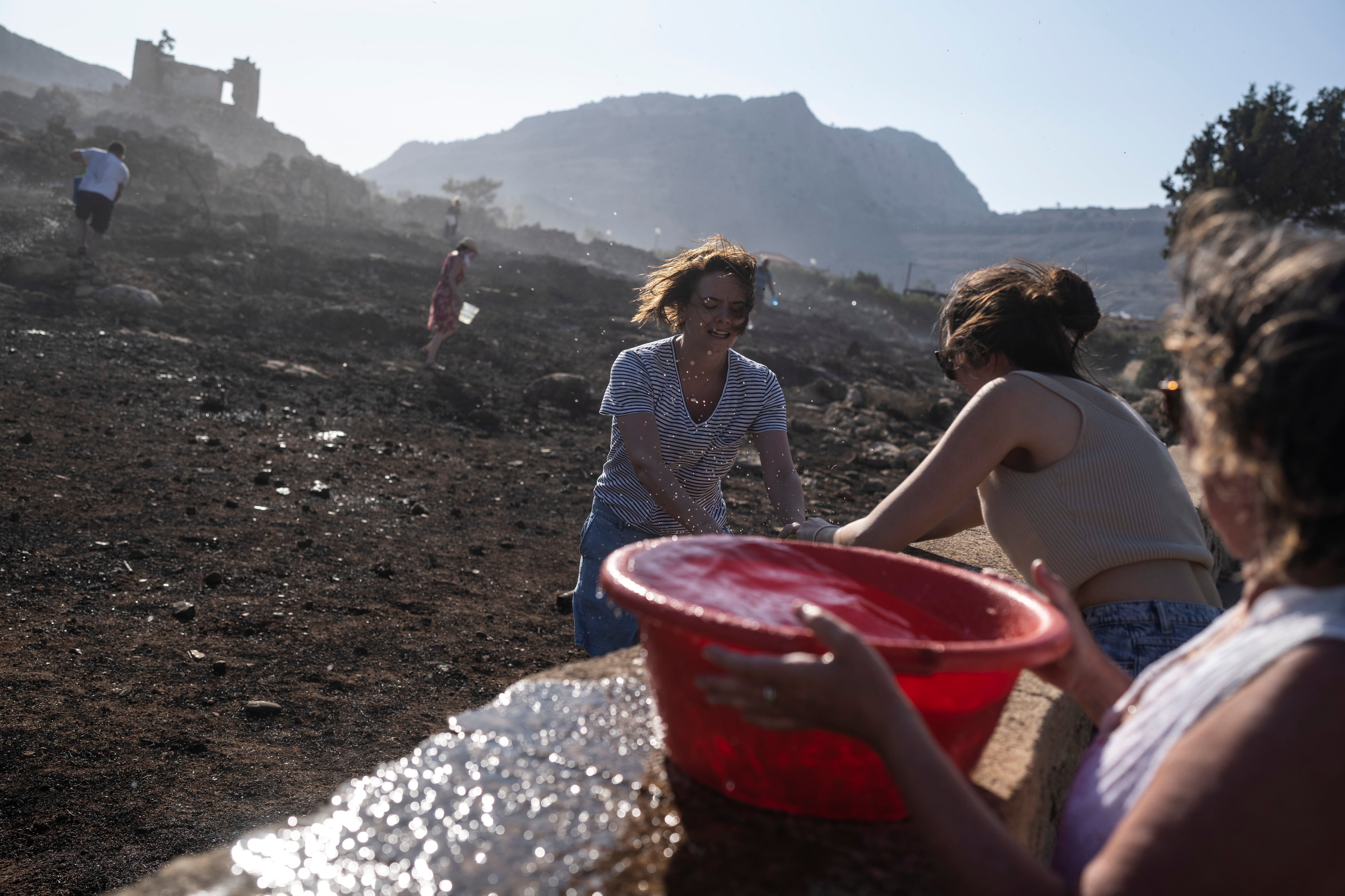 Turistas alemanes y residentes tratan de extinguir un incendio cerca del balneario costero de Lindos (AP Foto/Petros Giannakouris)