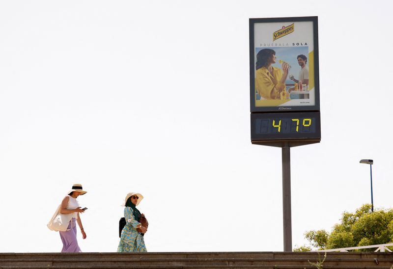 Dos personas pasan junto a un termómetro que marca 47 grados en una calle de Sevilla, España. 11 junio 2022. REUTERS/Marcelo del Pozo