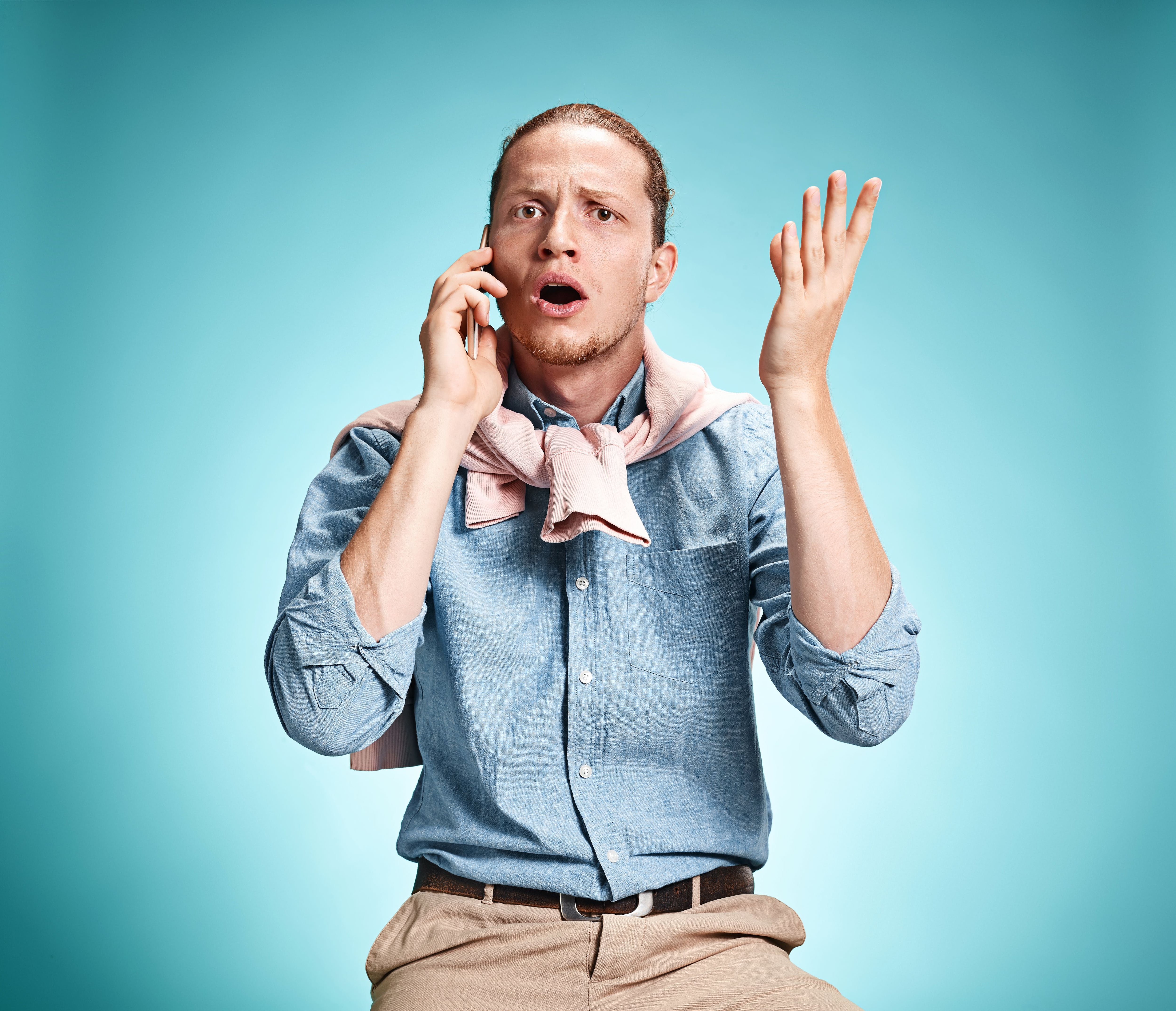 The young surprised caucasian businessman on blue background talking on cell phone