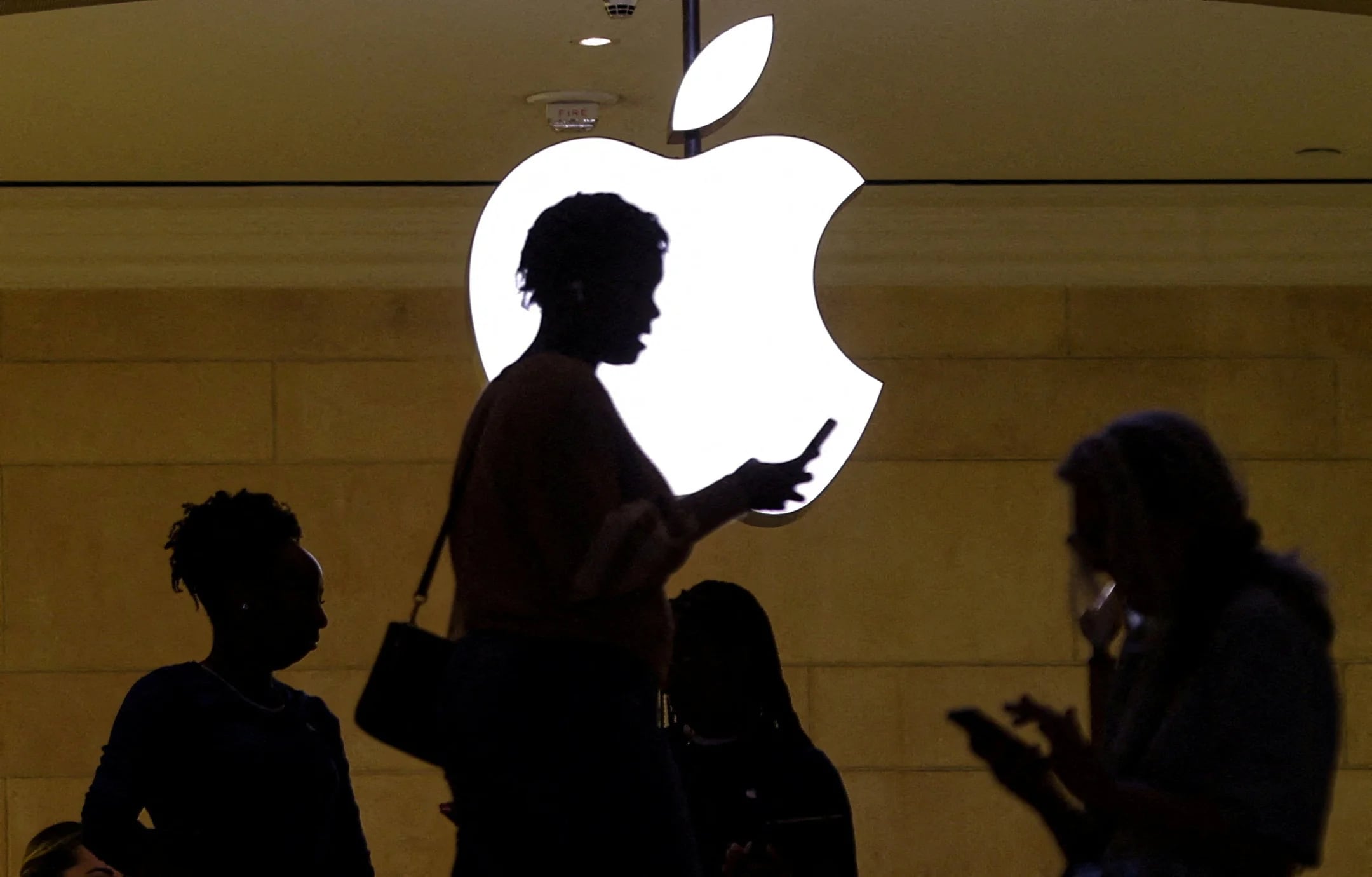 FILE PHOTO: A women uses an iPhone mobile device as she passes a lighted Apple logo at the Apple store at Grand Central Terminal in New York City, U.S., April 14, 2023. REUTERS/Mike Segar/File Photo