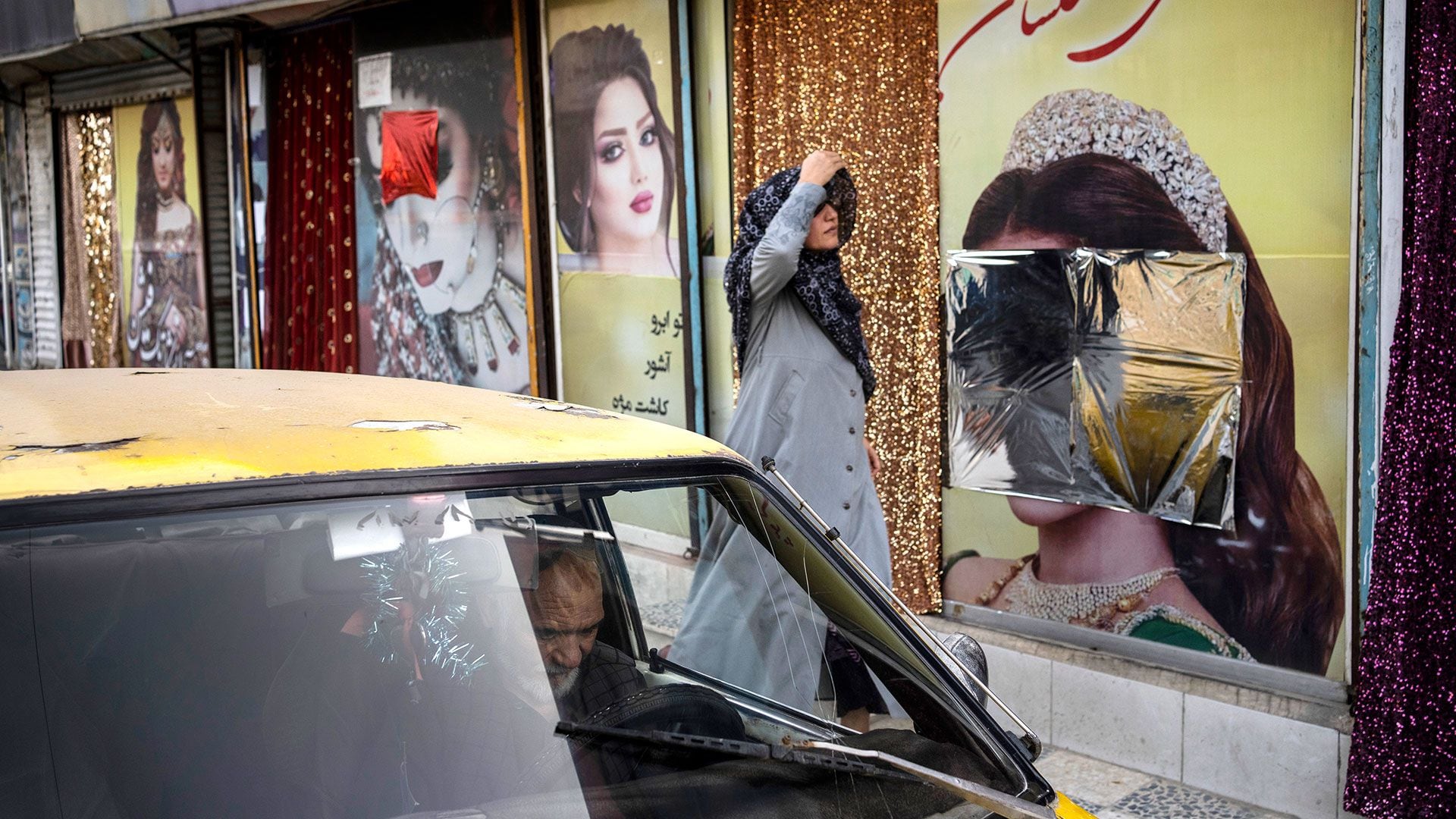 ARCHIVO - Una mujer pasa frente a un salón de belleza con adornos en las ventanas que han sido desfigurados en Kabul, Afganistán, el domingo 12 de septiembre de 2021. La fecha límite de un mes dada a la prohibición de los salones de belleza para mujeres en Afganistán finalizó el martes 25 de julio de 2023