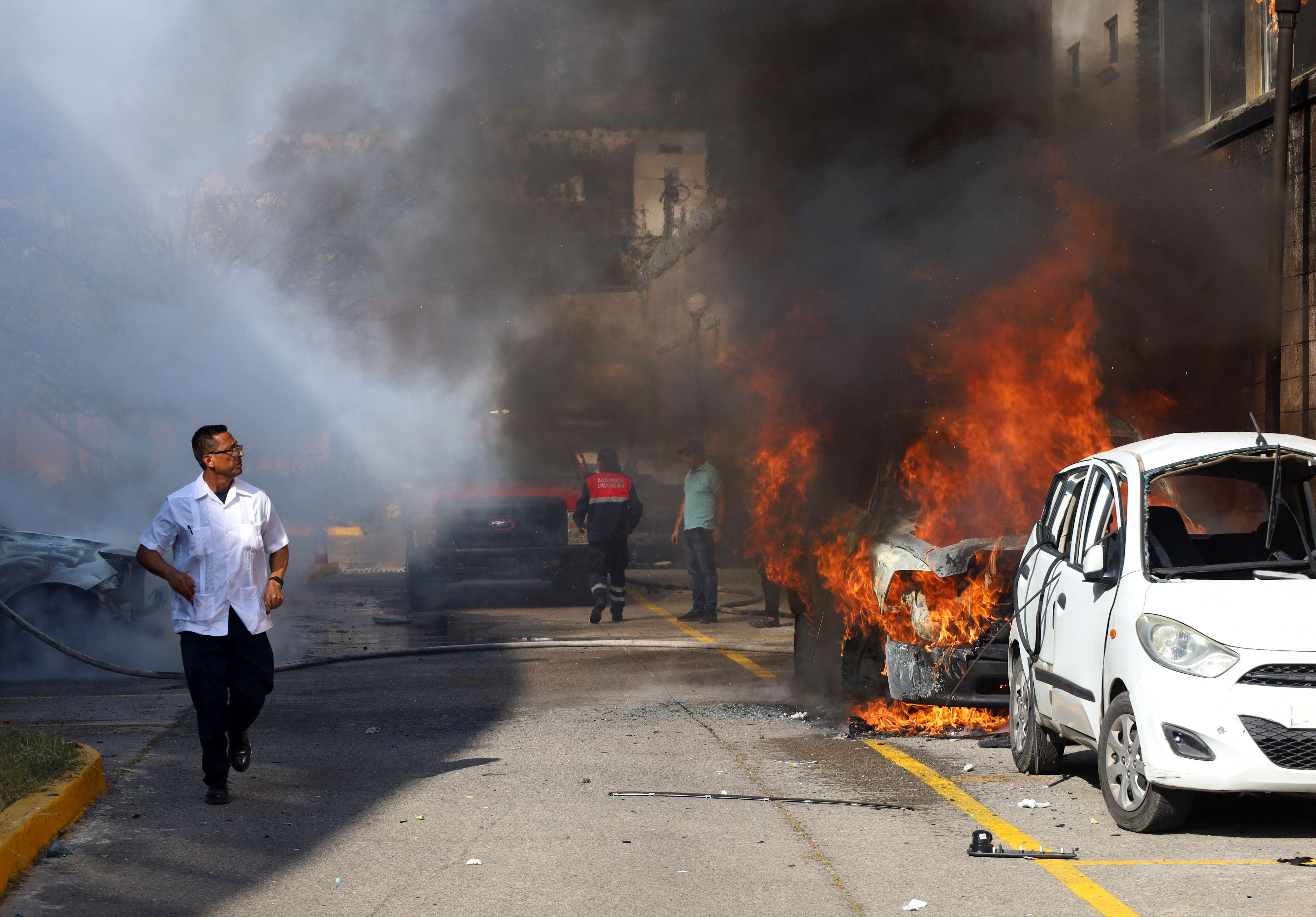 A man walks past vehicles on fire, after students from Ayotzinapa Teacher Training College threw petrol bombs at the facilities of Guerrero Government's Palace, during a protest to demand justice for their slain colleague Yanqui Kothan Gomez, in Chilpancingo, Mexico, April 8, 2024. REUTERS/Oscar Guerrero