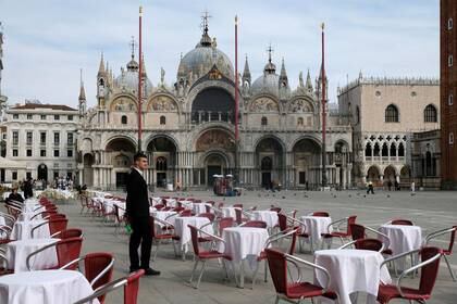 Un camarero de pie junto a mesas vacías frente a un restaurante en la Plaza de San Marcos de Venecia (REUTERS/Manuel Silvestri)
