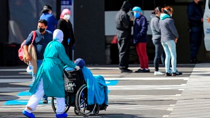 Familiares de pacientes diagnosticados con COVID-19 esperan información mientras ingresa un paciente en silla de ruedas, este lunes, en el hospital del Iess, en Quito (Ecuador). EFE/José Jácome