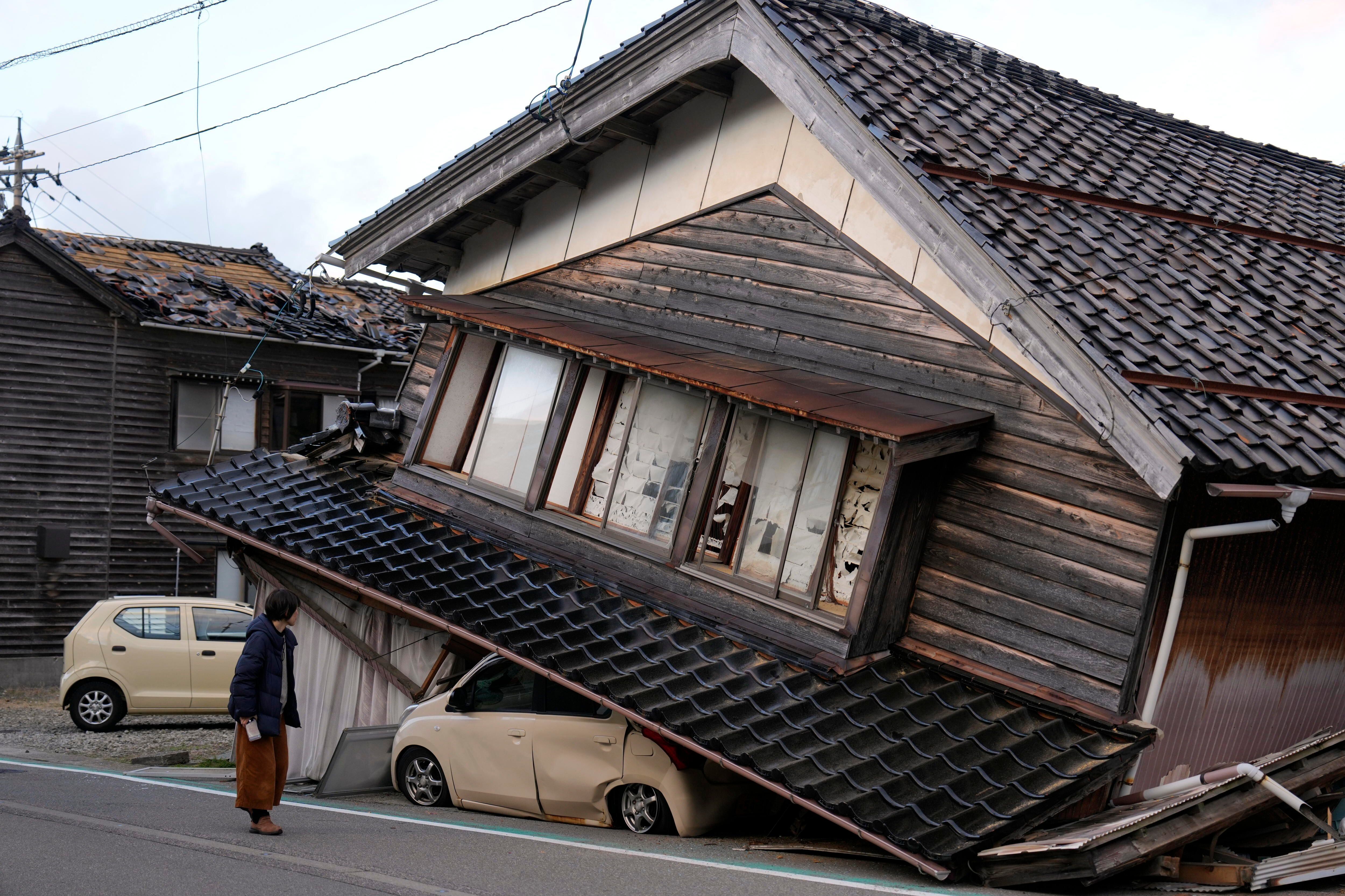 Una mujer observa una vivienda y vehículos dañados tras un fuerte terremoto en Tohi Town, en la península de Noto (EFE/FRANCK ROBICHON) 