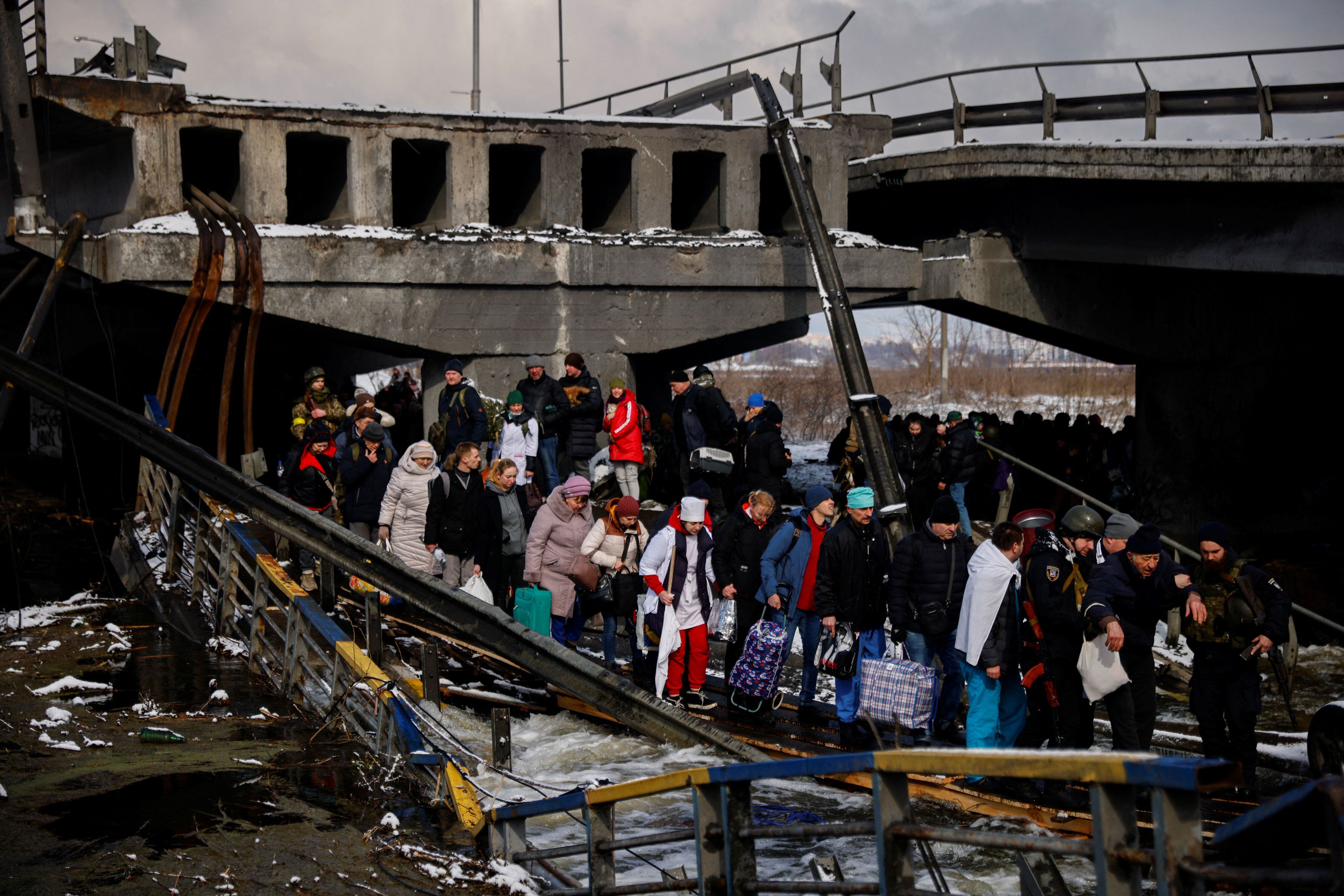 La gente cruza un río improvisado cruzando debajo de un puente destruido mientras huyen del avance de las tropas rusas cuyo ataque contra Ucrania continúa en la ciudad de Irpin en las afueras de Kiev, Ucrania, el 8 de marzo de 2022. (REUTERS/Thomas Peter)