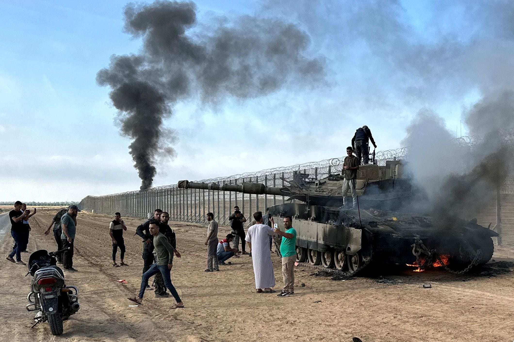 Palestinos celebran y observan un vehículo militar israelí arder tras ser alcanzado por terroristas de Hamas que se infiltraron en zonas del sur de Israel, este 7 de octubre de 2023 (Reuters)