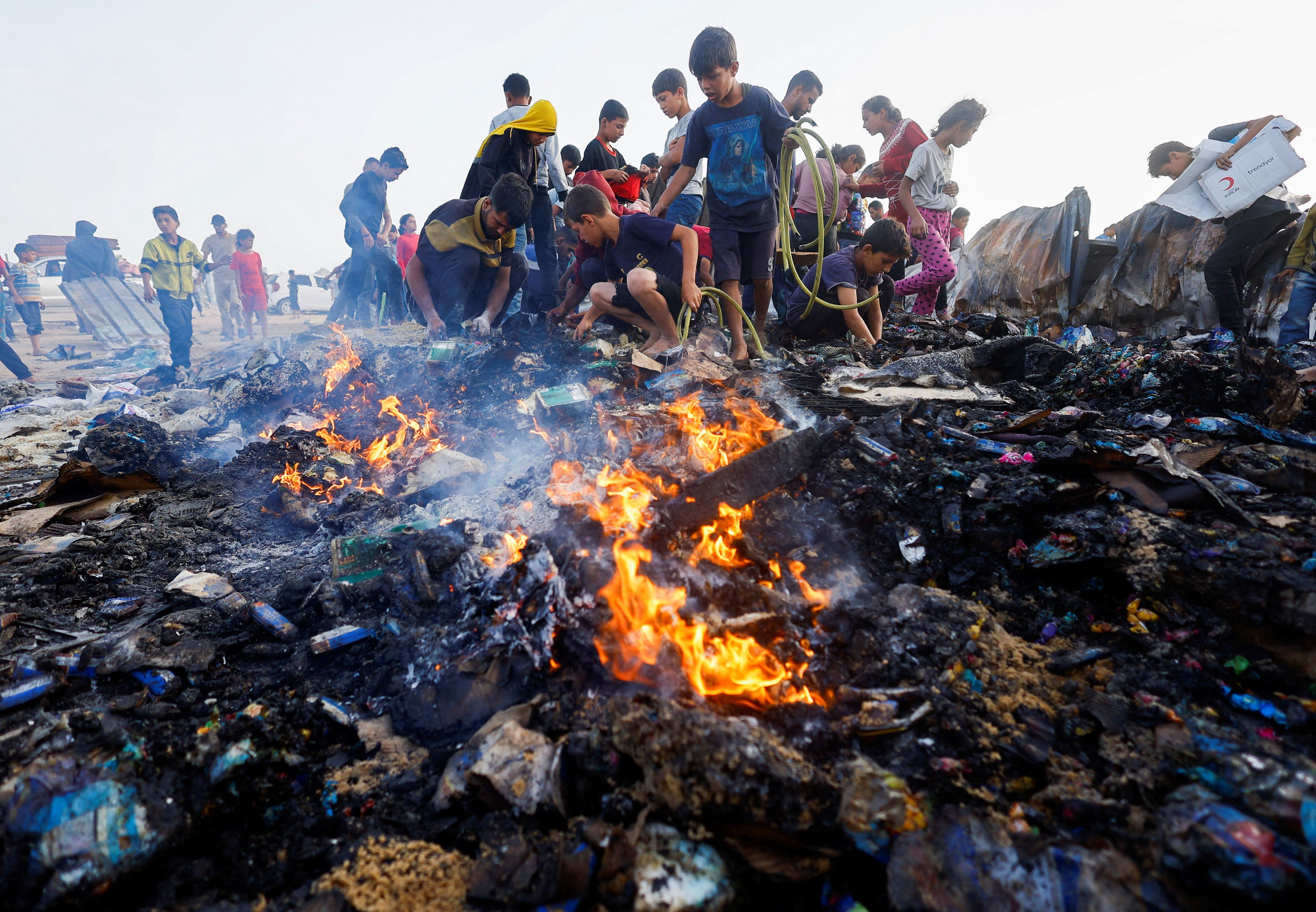 Palestinos buscan comida entre los escombros quemados tras el ataque israelí en una zona designada para desplazados, en Rafah (REUTERS/Mohammed Salem)
