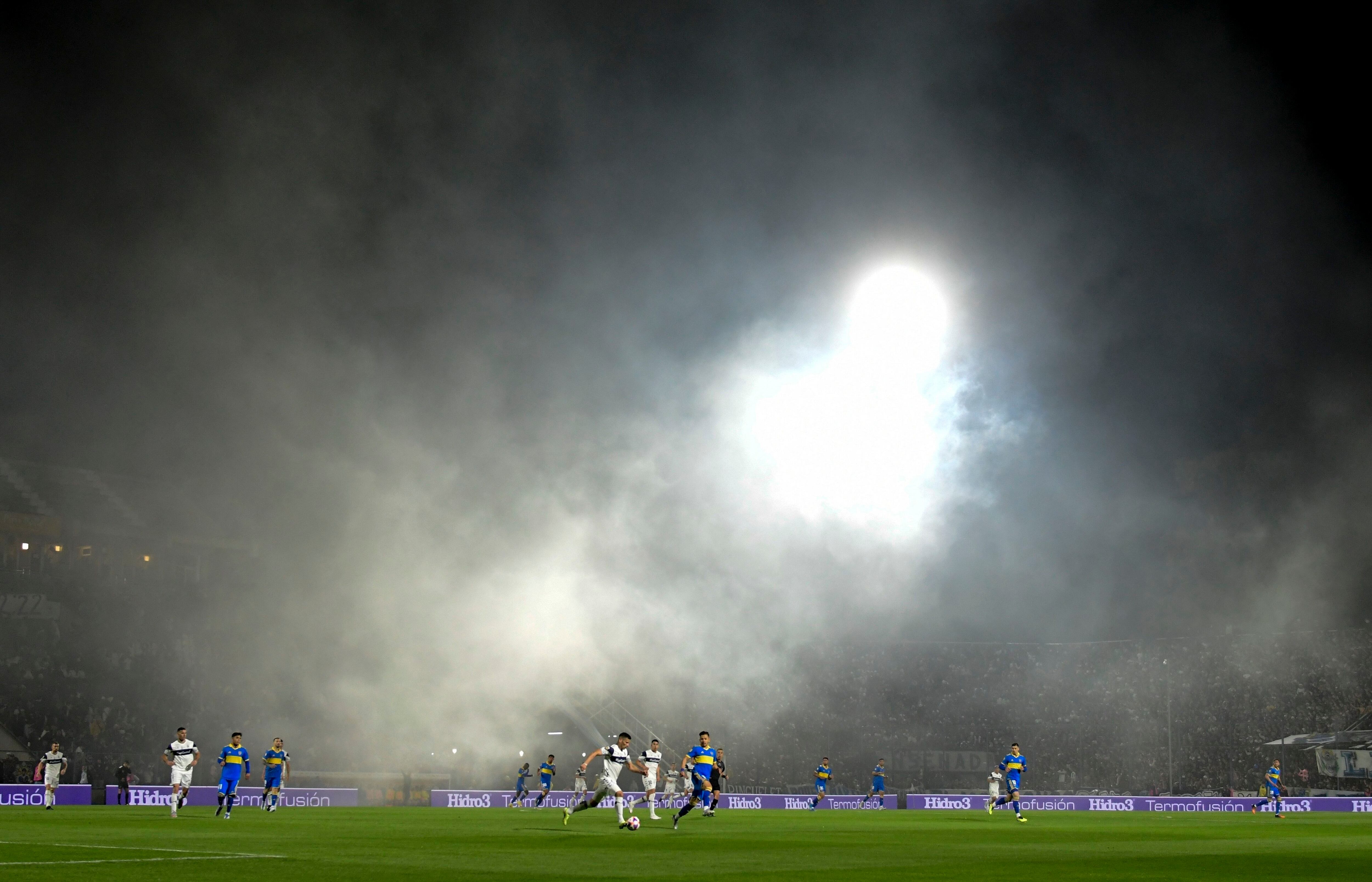 Jugadores de Gimnasia de la Plata y Boca Juniors juegan en medio de una nube de gases lacrimógenos, el 6 de octubre de 2022. El partido fue suspendido a los 9 minutos de empezar y por los incidentes murió un hombre de 56 años llamado César Regueiro, que sufrió un paro cardíaco (AP Foto/Gustavo Garello)