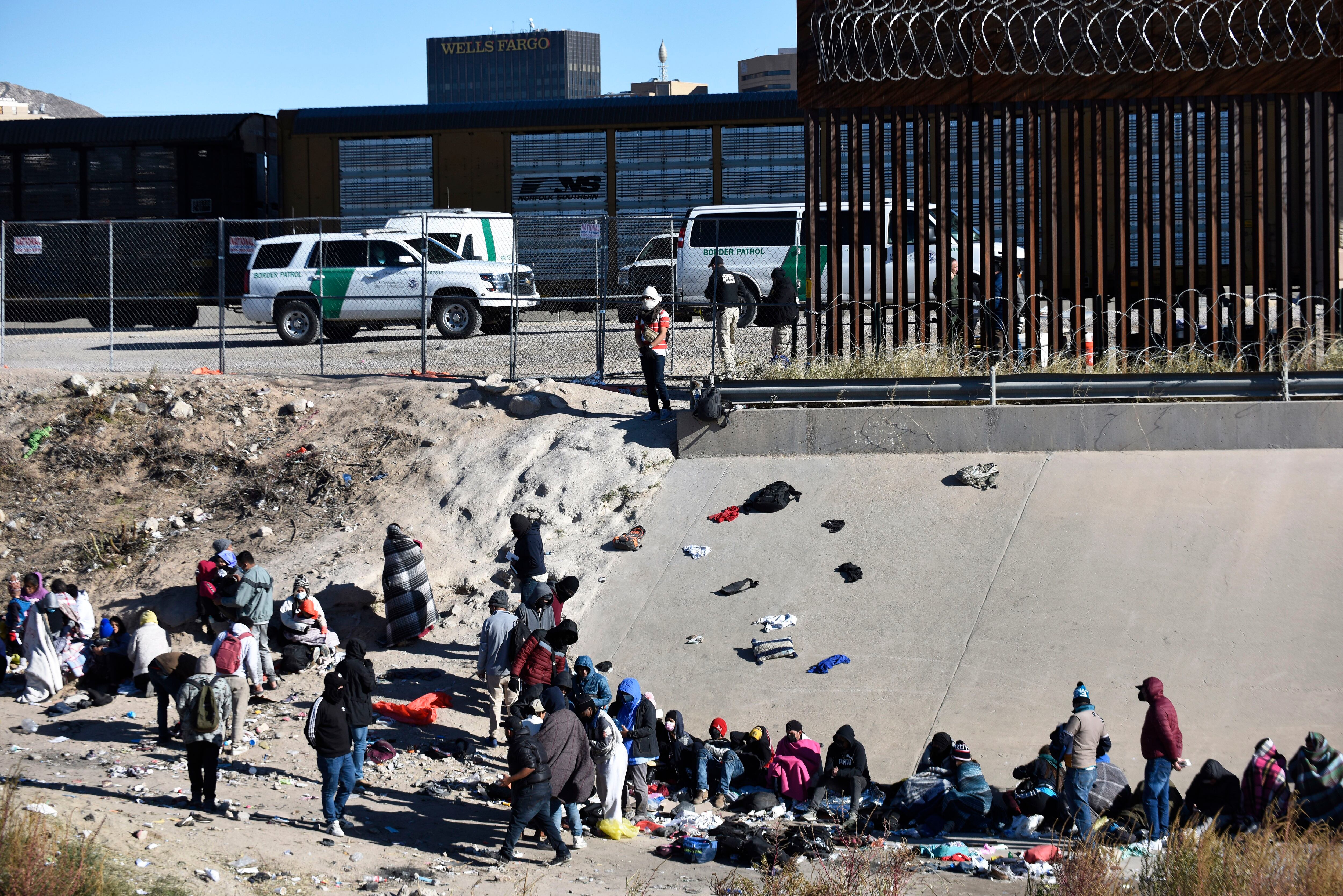 Migrantes esperan a cruzar la frontera entre Estados Unidos y México, el miércoles 14 de diciembre de 2022, desde Ciudad Juárez, México, frente a vehículos de la Patrulla Fronteriza en El Paso, Texas  (AP/Christian Chávez)