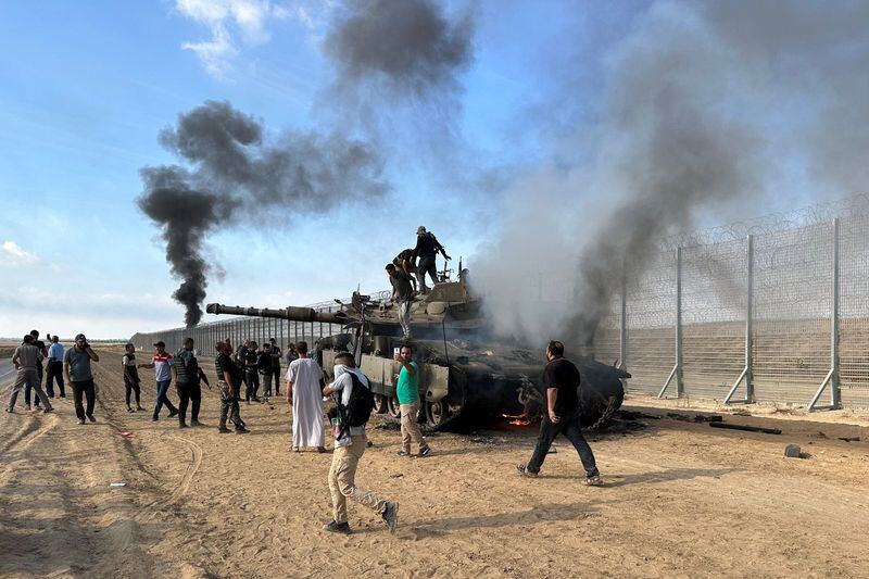 Palestinos reaccionan mientras un vehículo militar israelí arde tras ser alcanzado por atacantes que se infiltraron en zonas del sur de Israel (Reuters)