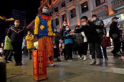 Un niño trata de embocar unos palillos en un recipiente en una calle comercial de Wuhan el 15 de enero del 2021. La vida se normalizó en la ciudad donde estalló el brote de coronavirus hace un año. (AP Photo/Ng Han Guan, File)