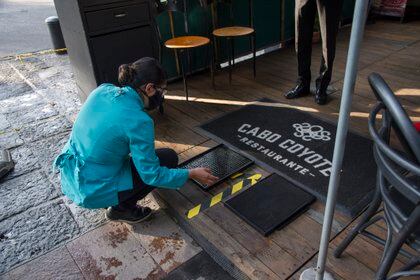 Alfombras sanitizantes en la entrada de un restaurante (Photo by CLAUDIO CRUZ / AFP)