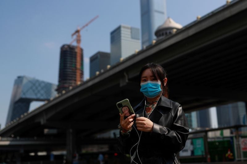 Una mujer usa su smartphone mientras camina por el Distrito Central de Negocios de Pekín en China, 17 de abril de 2020. REUTERS/Thomas Peter