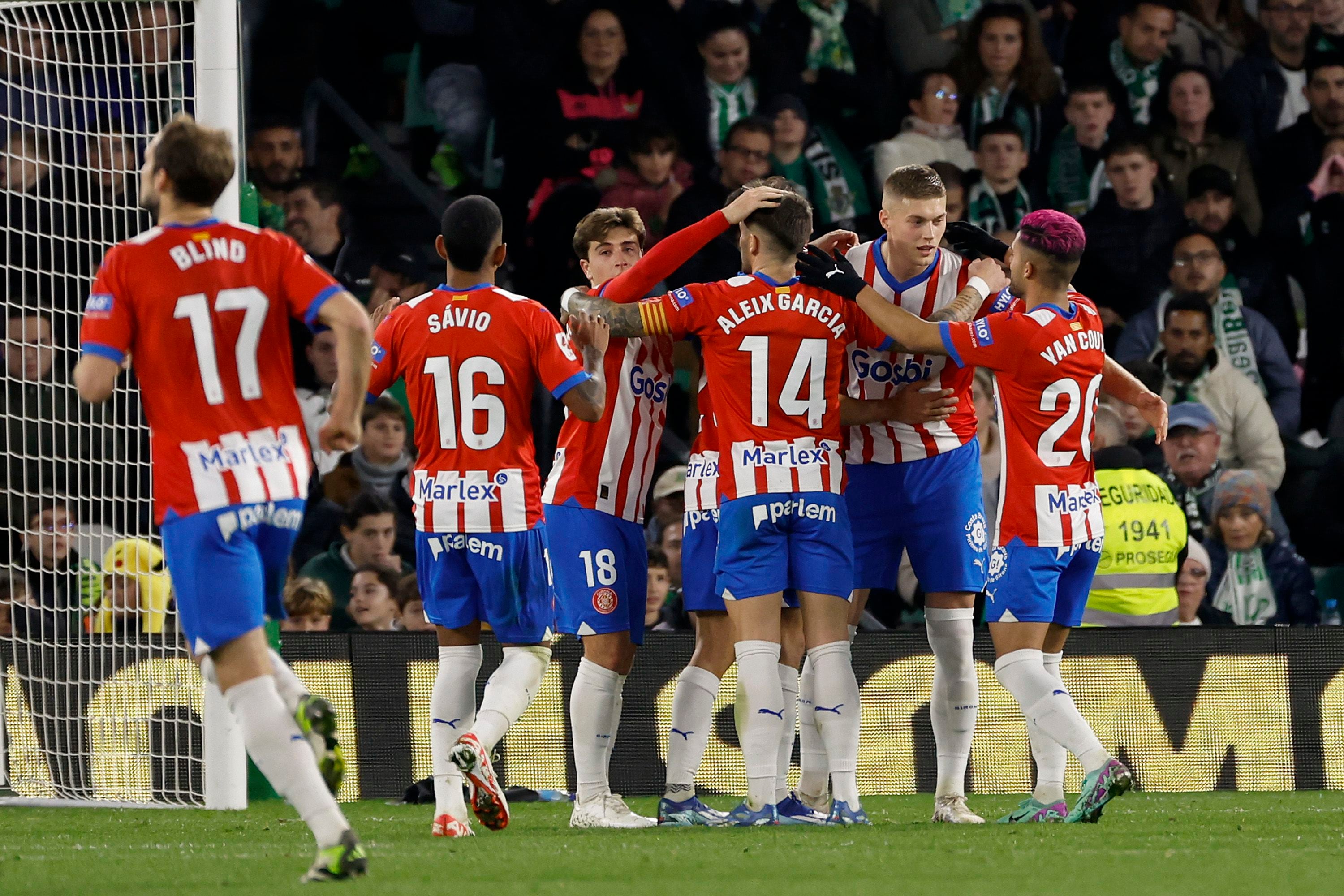 El delantero ucraniano del Girona FC Artem Dovbyk celebra junto a sus compañeros tras abrir el marcador durante un encuentro correspondiente a la jornada 18 de LaLiga que estos dos equipos jugaron en el estadio Benito Villamarín de Sevilla (EFE / Julio Muñoz) 