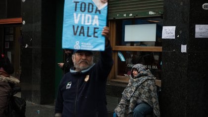 Una persona sin techo es vista detrás de un cartel con la leyenda "Toda Vida Vale" (Adrián Escandar)