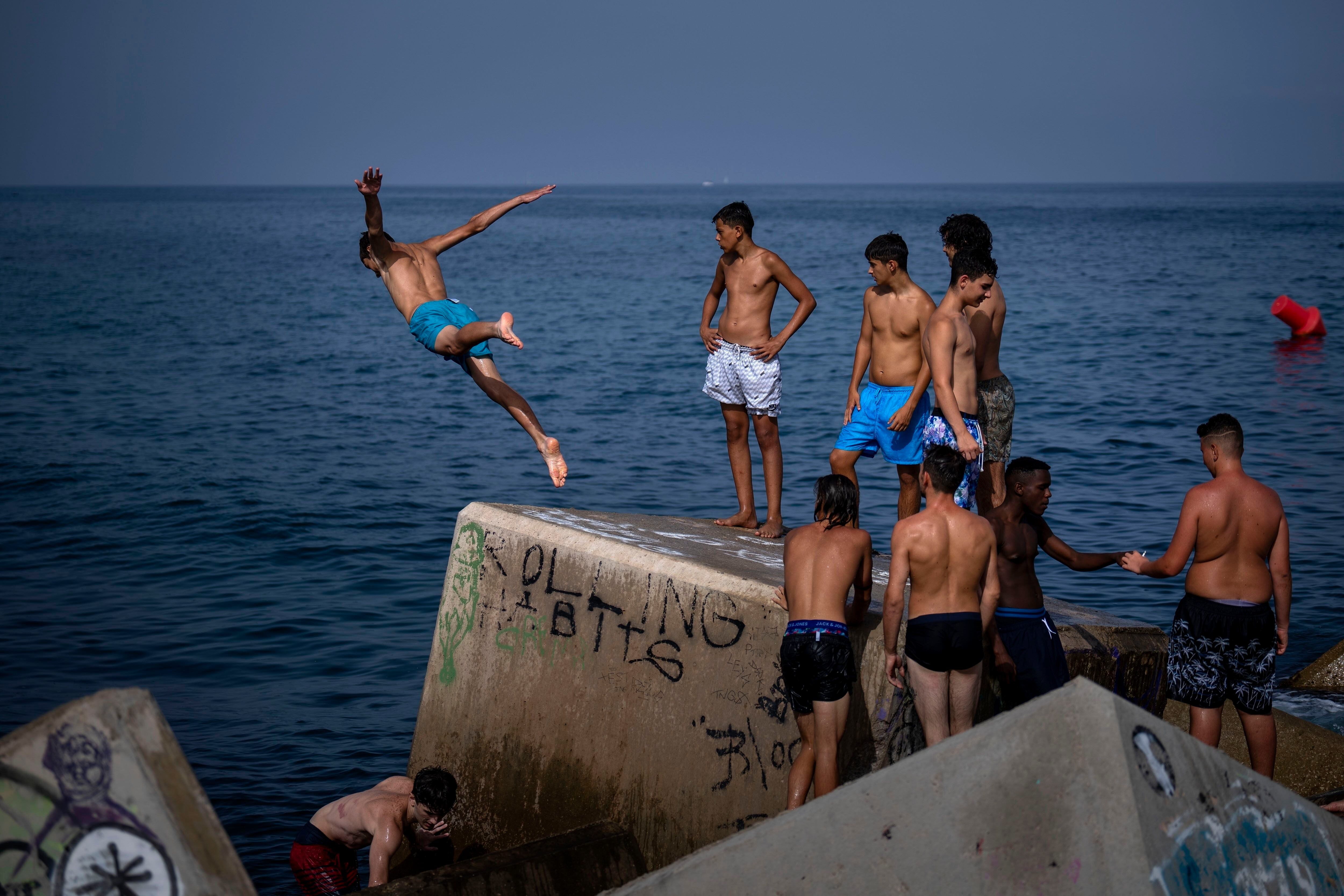 Un hombre salta al mar desde un rompeolas en Barcelona, España (AP Foto/Emilio Morenatti)