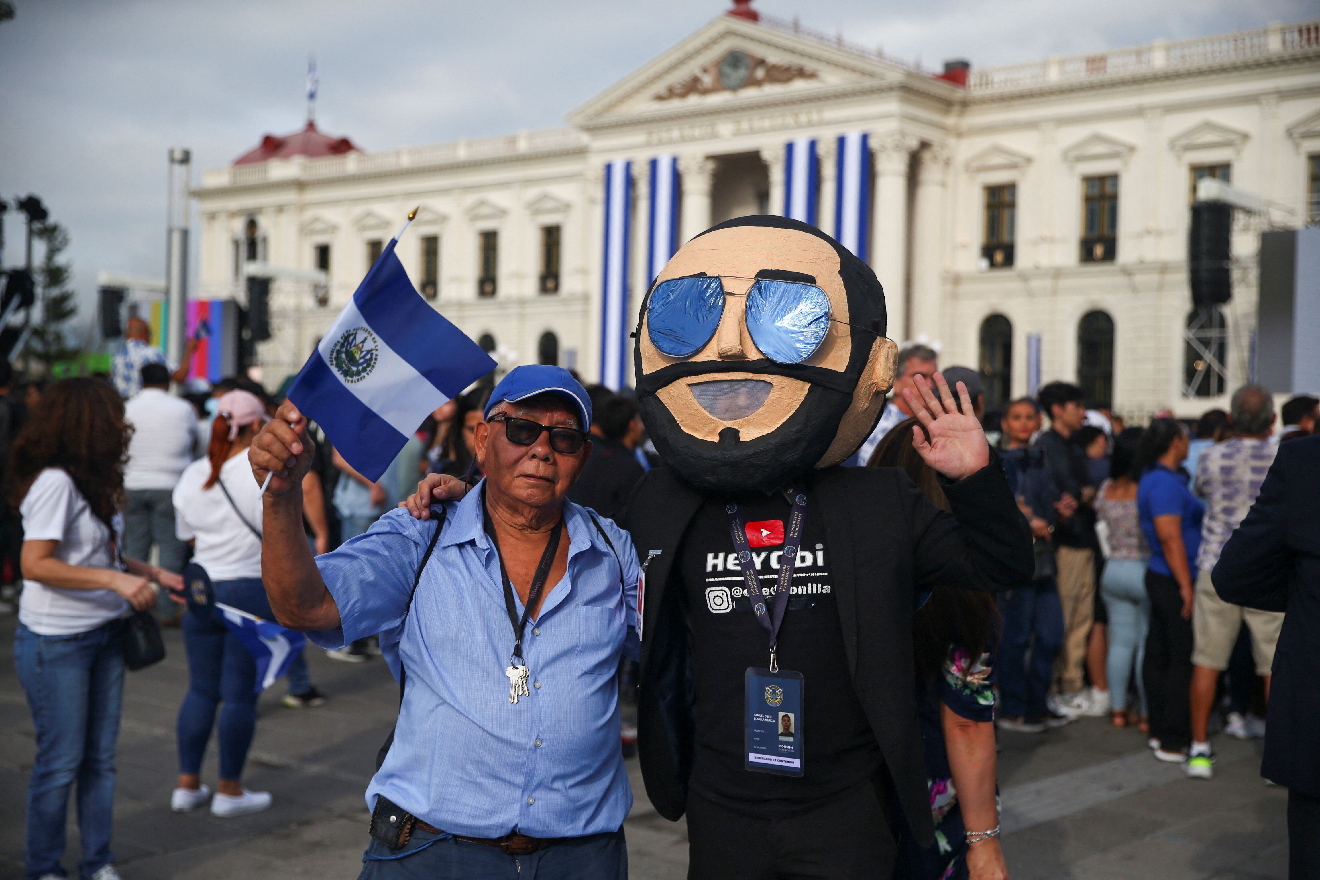 Una persona lleva una máscara que representa al presidente de El Salvador, Nayib Bukele, mientras la gente llega a su ceremonia de investidura para el segundo mandato, en San Salvador (REUTERS/Jose Cabezas)