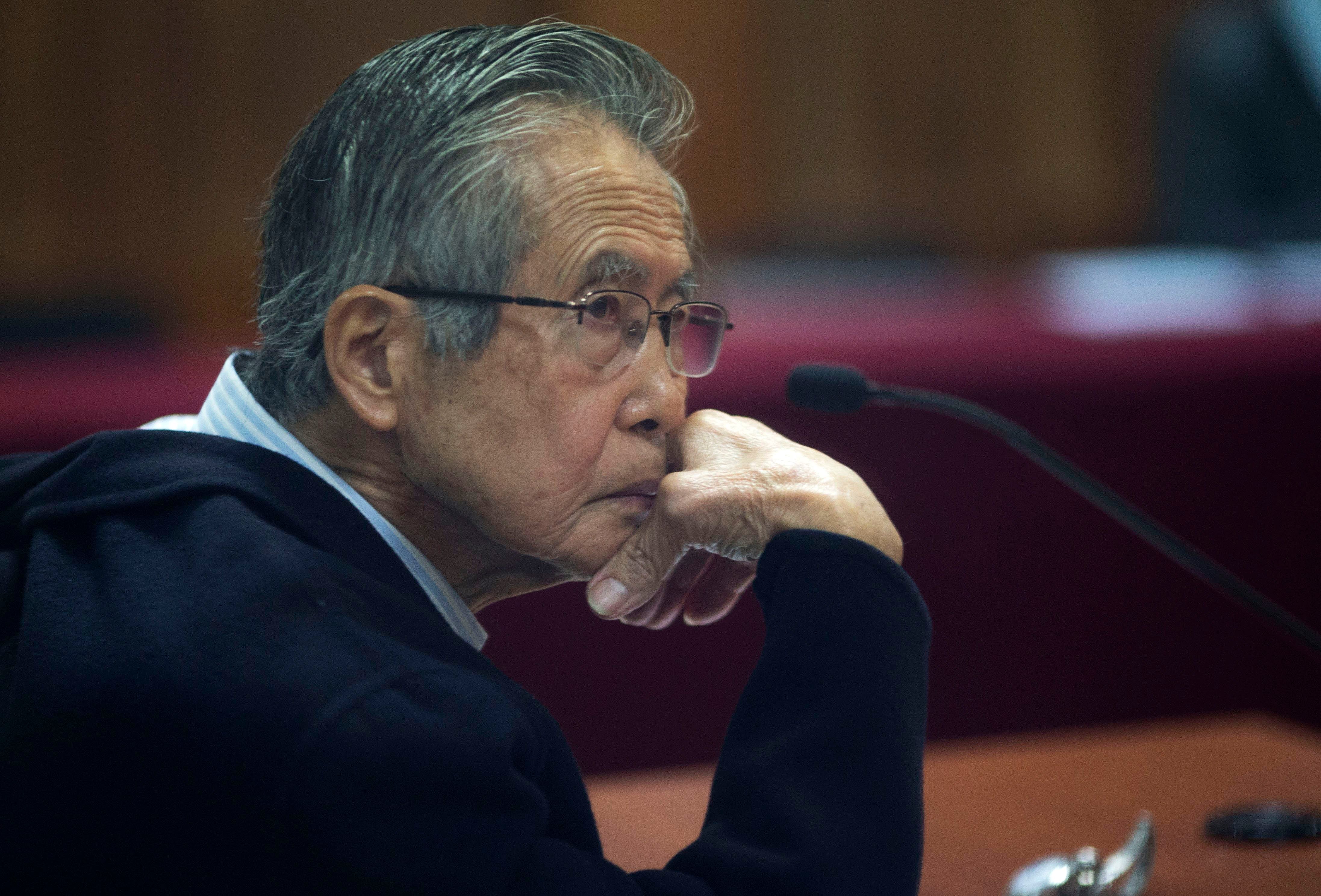 ARCHIVO - El encarcelado expresidente peruano Alberto Fujimori, fotografiado a través de una ventana de vidrio, asiste a su juicio en una base policial en las afueras de Lima, Perú, el 28 de junio de 2016. La agencia carcelaria de Perú dijo el lunes 7 de agosto de 2023 que Fujimori salió de prisión para ir al dentista tras la difusión de un video donde se lo ve bajar de una ambulancia y e ingresar caminando sin grilletes a un centro de belleza. (AP Foto/Martín Mejía, Archivo)