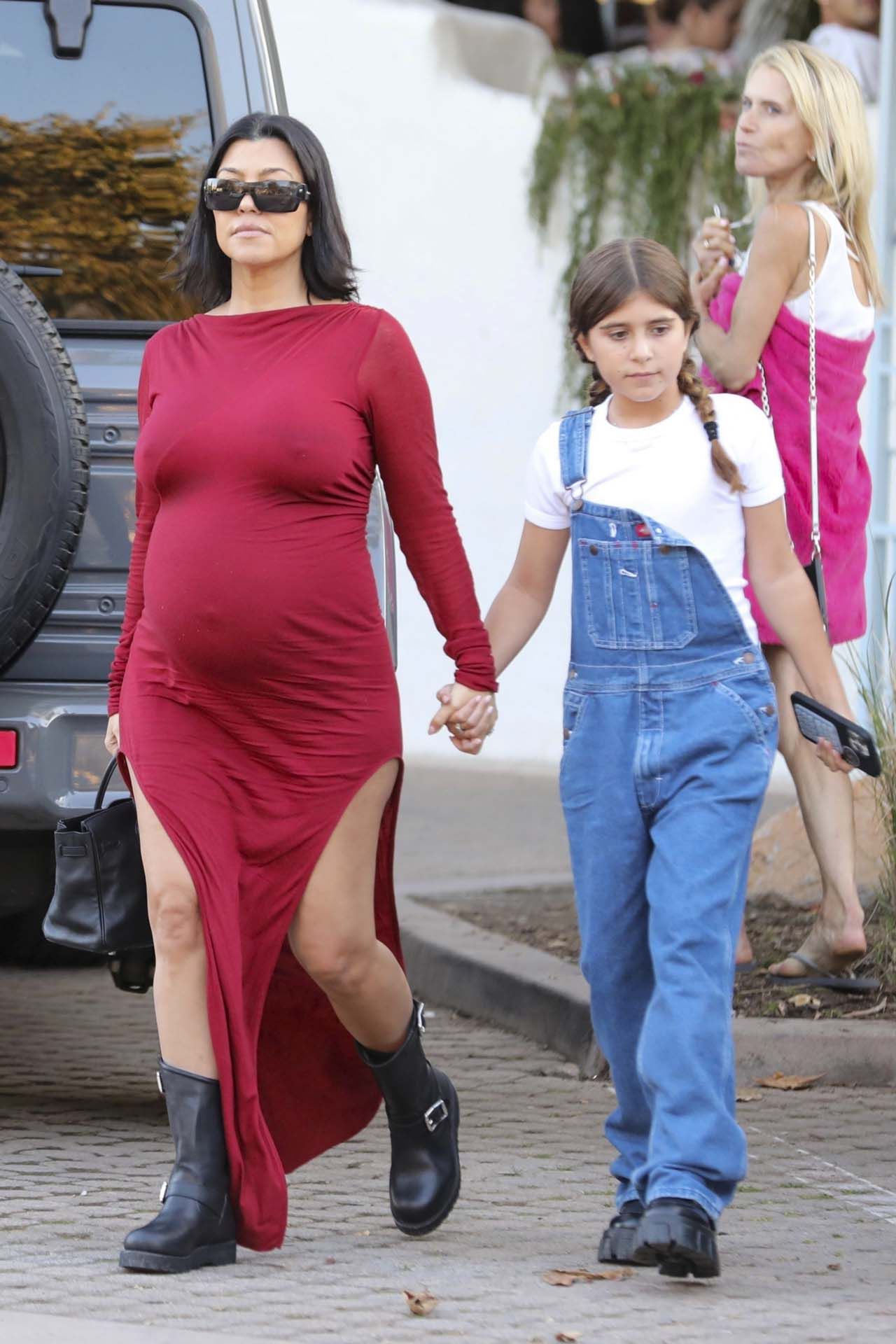 Kourtney Kardashian mostró su embarazo mientras paseaba junto a su hija Penelope. Lució un vestido rojo de mangas largas y con dos tajos en sus piernas. Además, llevó botas negras y lentes de sol