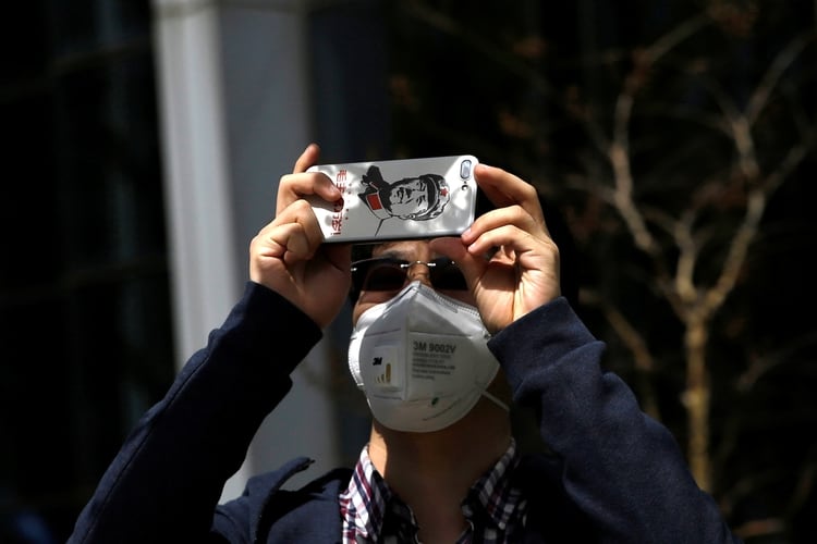 Un hombre usando una mascarilla facial mientras uso su teléfono inteligente en China REUTERS/Tingshu Wang
