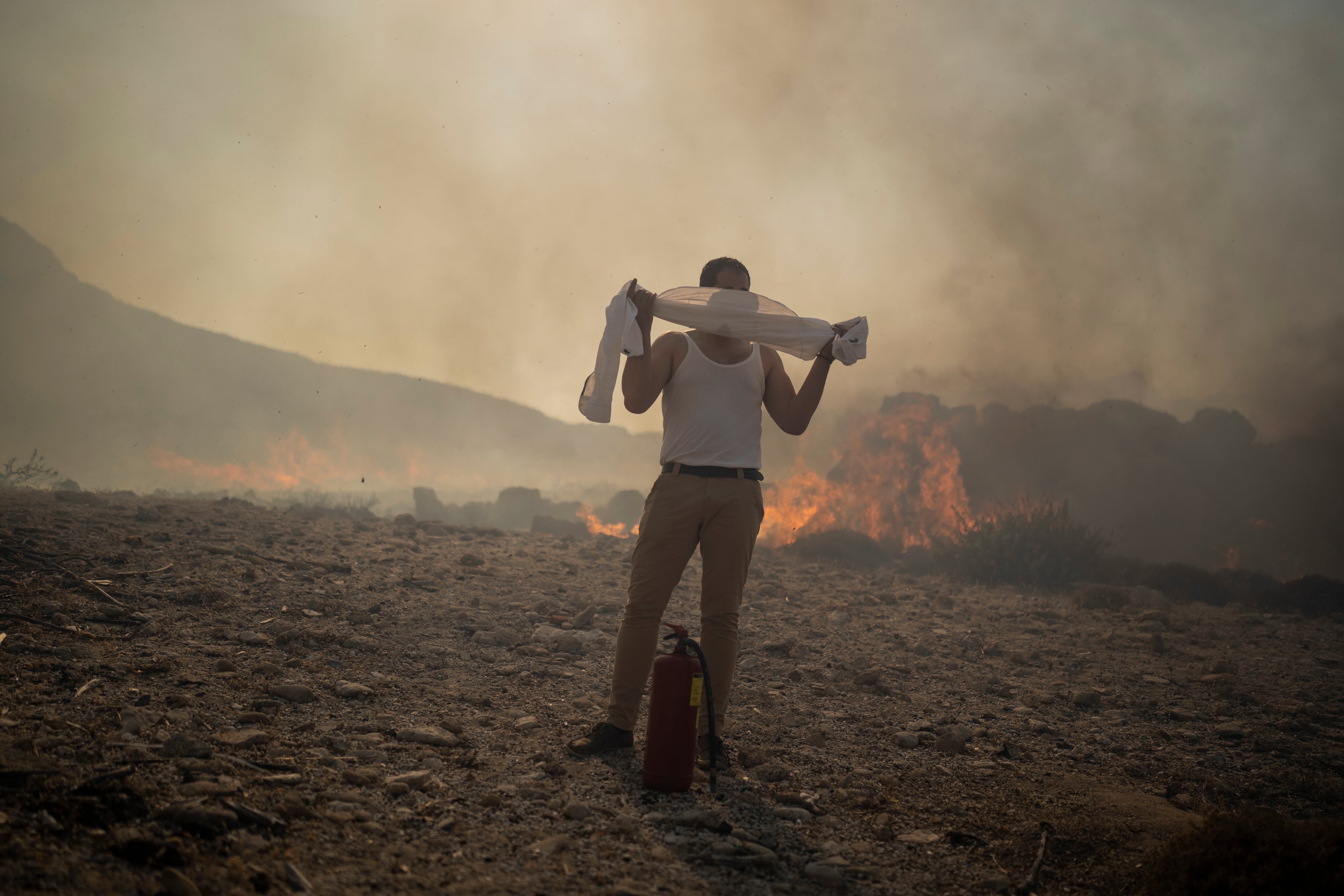 Un hombre se tapa el rostro con su camisa mientras trata de extinguir un incendio cerca del balneario costero de Lindos (AP Foto/Petros Giannakouris)