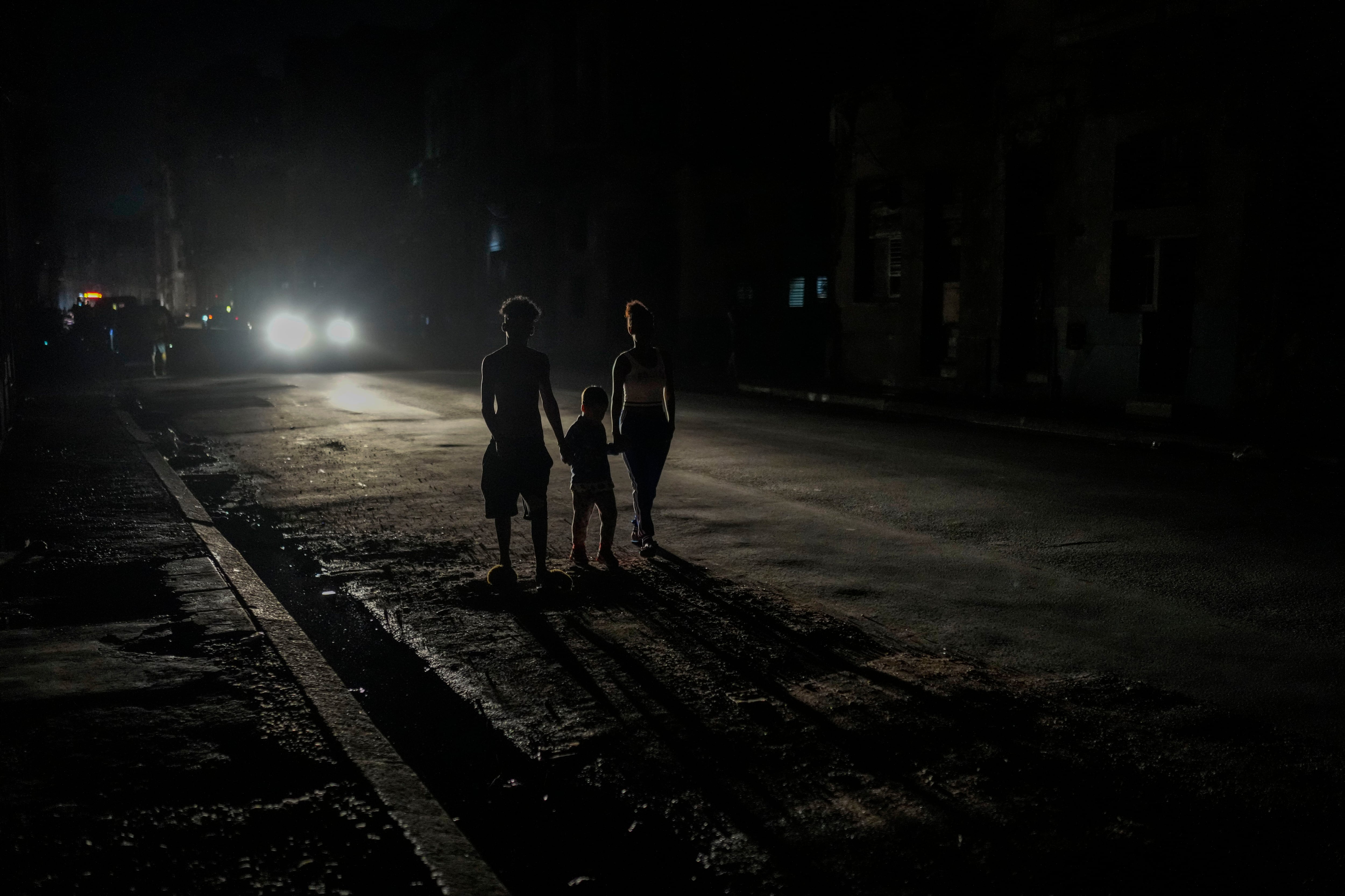 Varios residentes iluminados por las luces de un vehículo durante el apagón masivo (AP Foto/Ramón Espinosa)