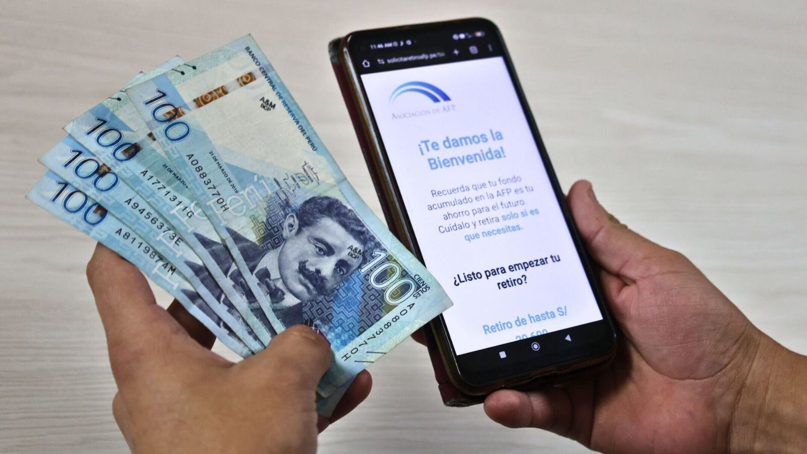 mano con billetes de 100 soles y celular con página de Asociación AFP