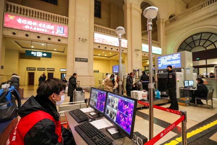 Funcionarios de seguridad de una estación de trenes de Wuhan portan mascarillas para protegerse en puestos de control, mientras revisan la temperatura de los pasajeros (Reuters)