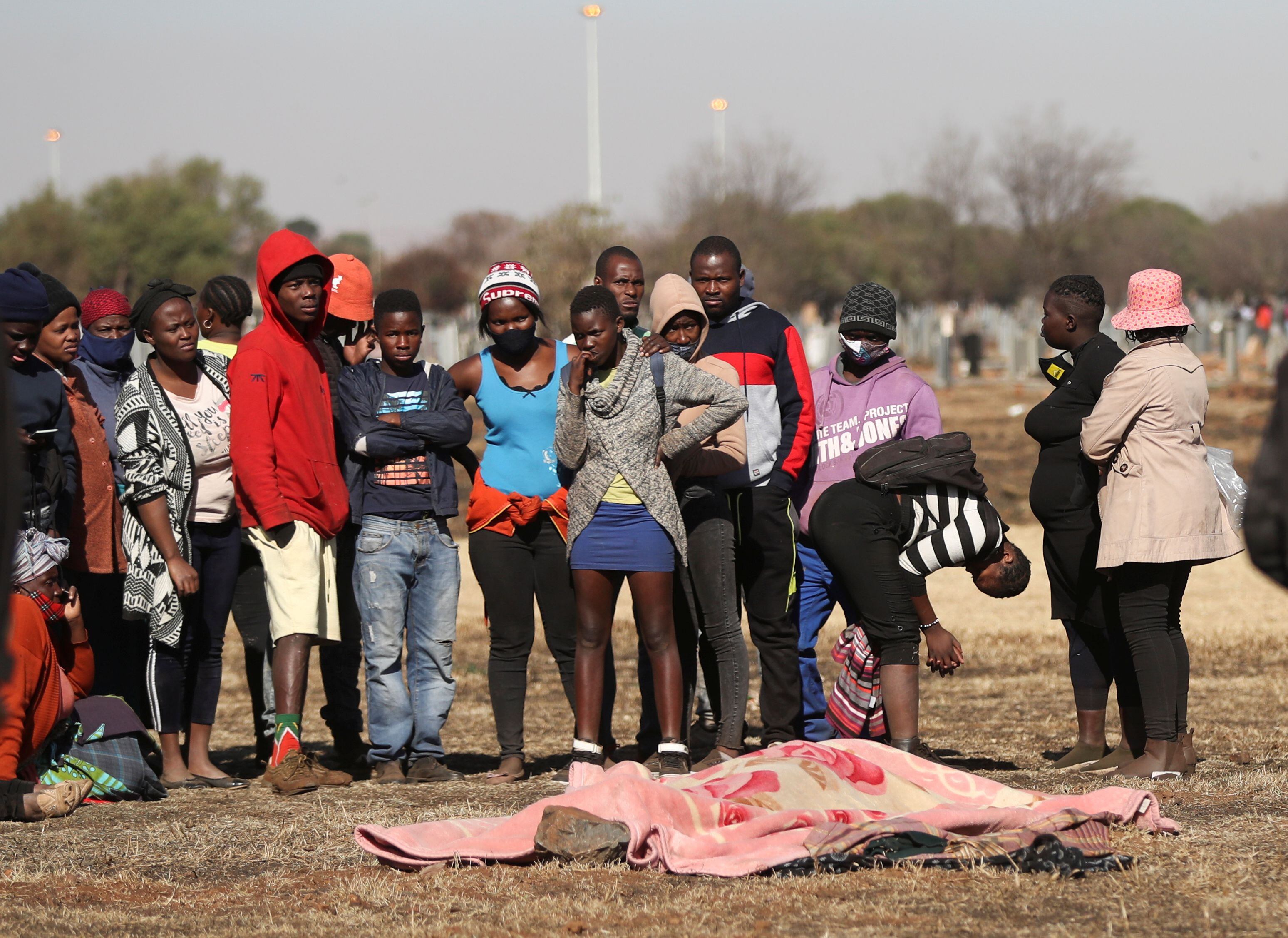 Lugareños y familiares junto al cuerpo de Vusi Dlamini, de 15 años, a quien supuestamente le dispararon fuera de un centro comercial donde se estaban llevando a cabo los saqueos. Vosloorus, Sudáfrica, 14 de julio de 2021. REUTERS / Siphiwe Sibeko