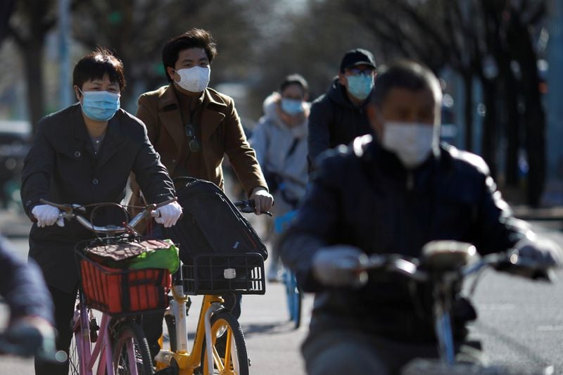 Varias personas montan bicicletas portando mascarillas para protegerse de coronavirus en Pekín. Marzo, 2020. REUTERS/Carlos Garcia Rawlins