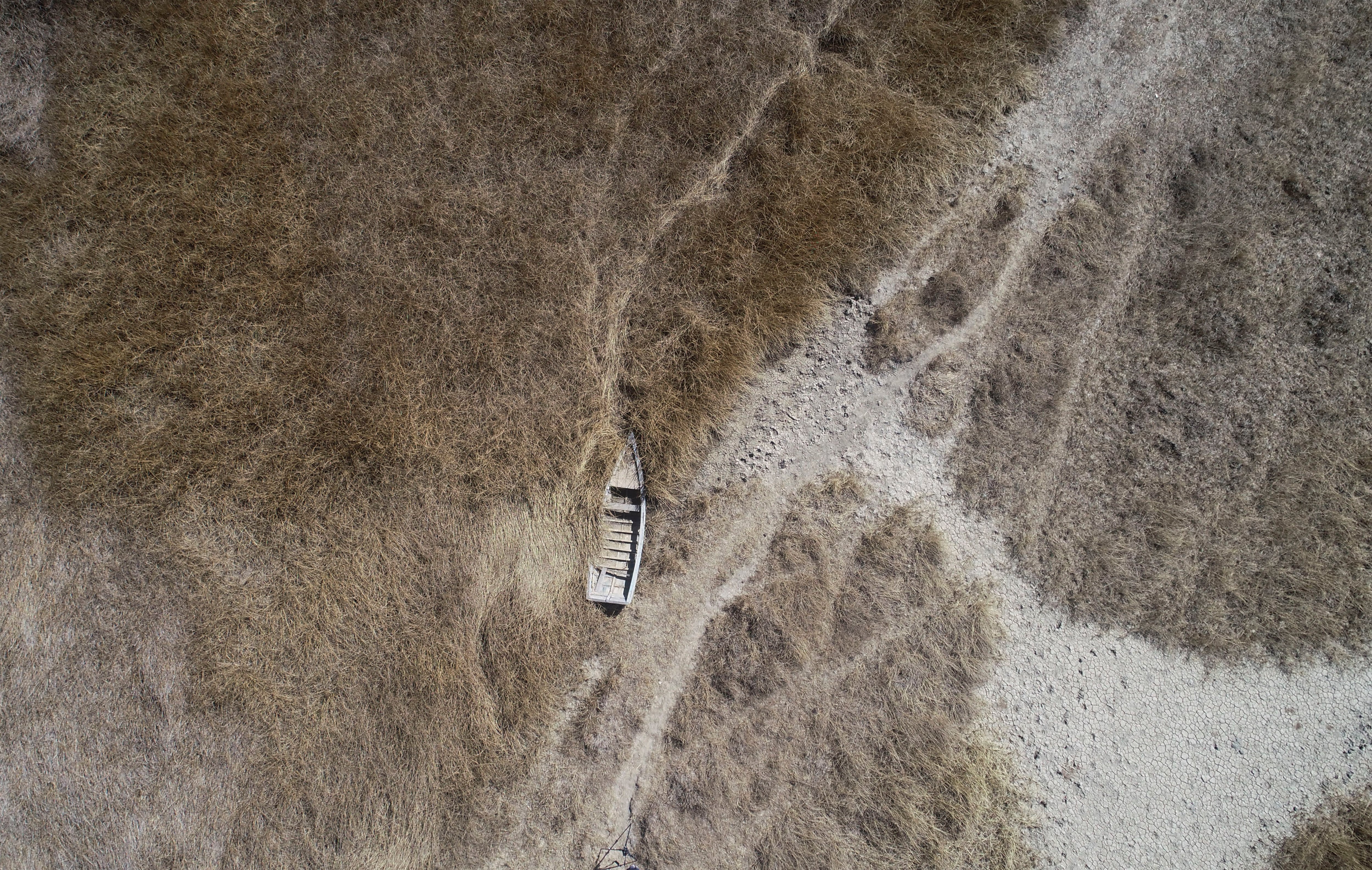 En la imagen, vista aérea de una embarcación abandonada cerca de la orilla del lago Titicaca, en Huarina, Bolivia, el 27 de julio de 2023. El bajo nivel del agua en el lago está teniendo un impacto directo en la flora y la fauna locales y afecta a las comunidades locales que dependen de la frontera natural entre Perú y Bolivia para su sustento. (AP Foto/Juan Karita)