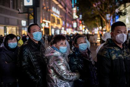 Personas con barbijos se paran alrededor de una pantalla gigante en 3D en la calle Jianghan en Wuhan el 10 de enero de 2021 (Foto de NICOLAS ASFOURI / AFP)