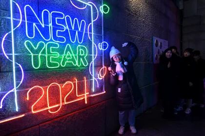 Una mujer posa para una fotografía frente a un cartel luminoso de 2024 antes de un evento de cuenta regresiva para celebrar el Año Nuevo en el centro de Seúl, el 31 de diciembre de 2023. (Foto de Jung Yeon-je / AFP)
