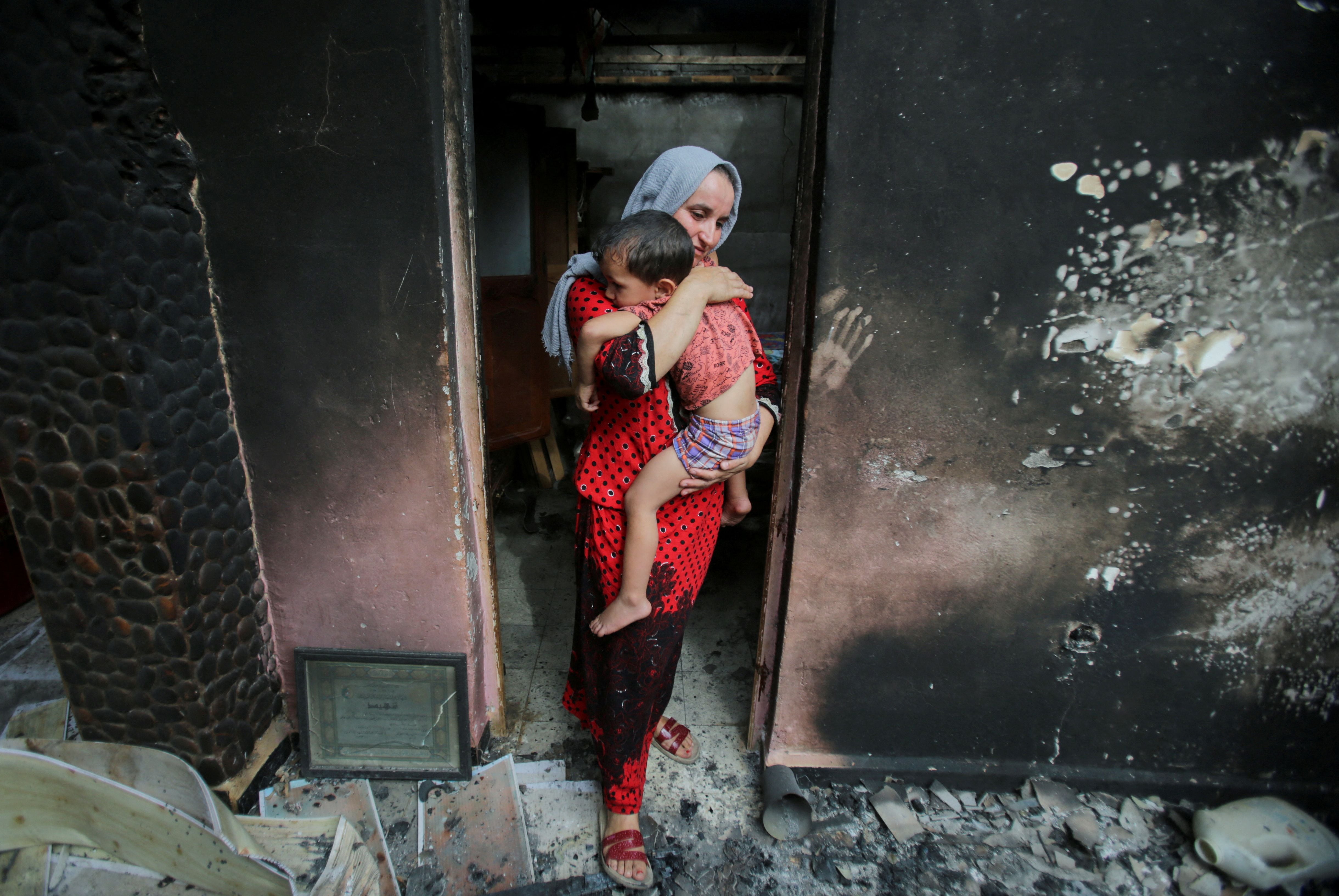 Una mujer lleva a su hijo dentro de su casa quemada, tras un incendio forestal en Bejaia, Argelia (REUTERS/Ramzi Boudina)