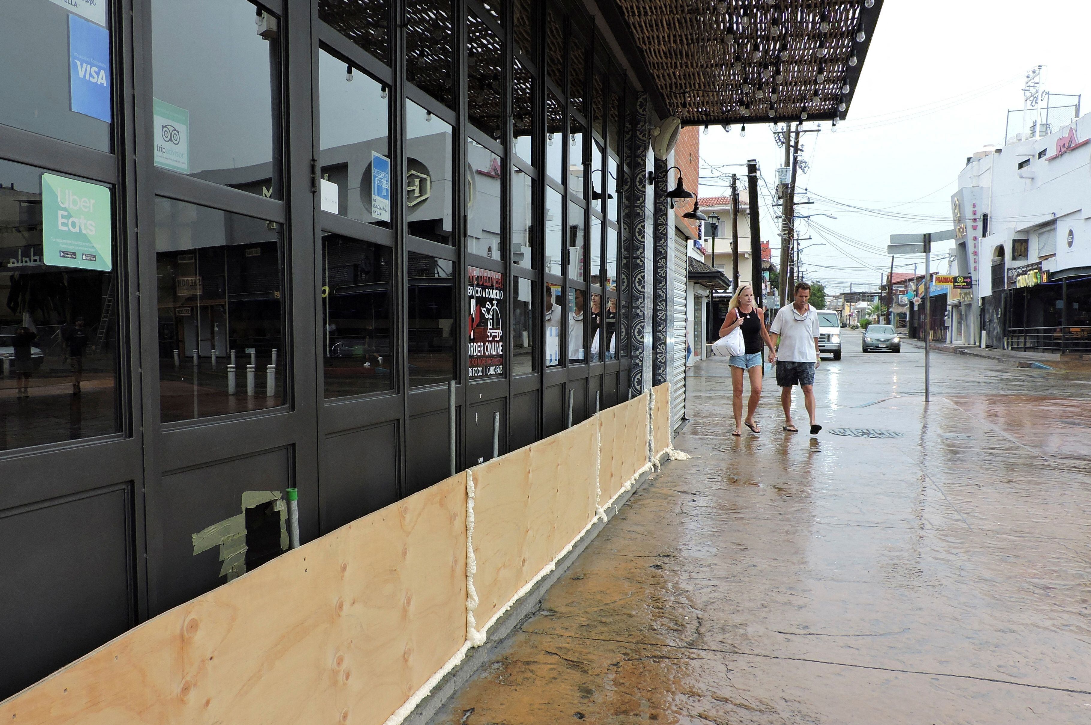 Los turistas caminan por un restaurante con una protección de madera para evitar ser afectados por inundaciones mientras el huracán Hilary. REUTERS/Monserrat Zavala 